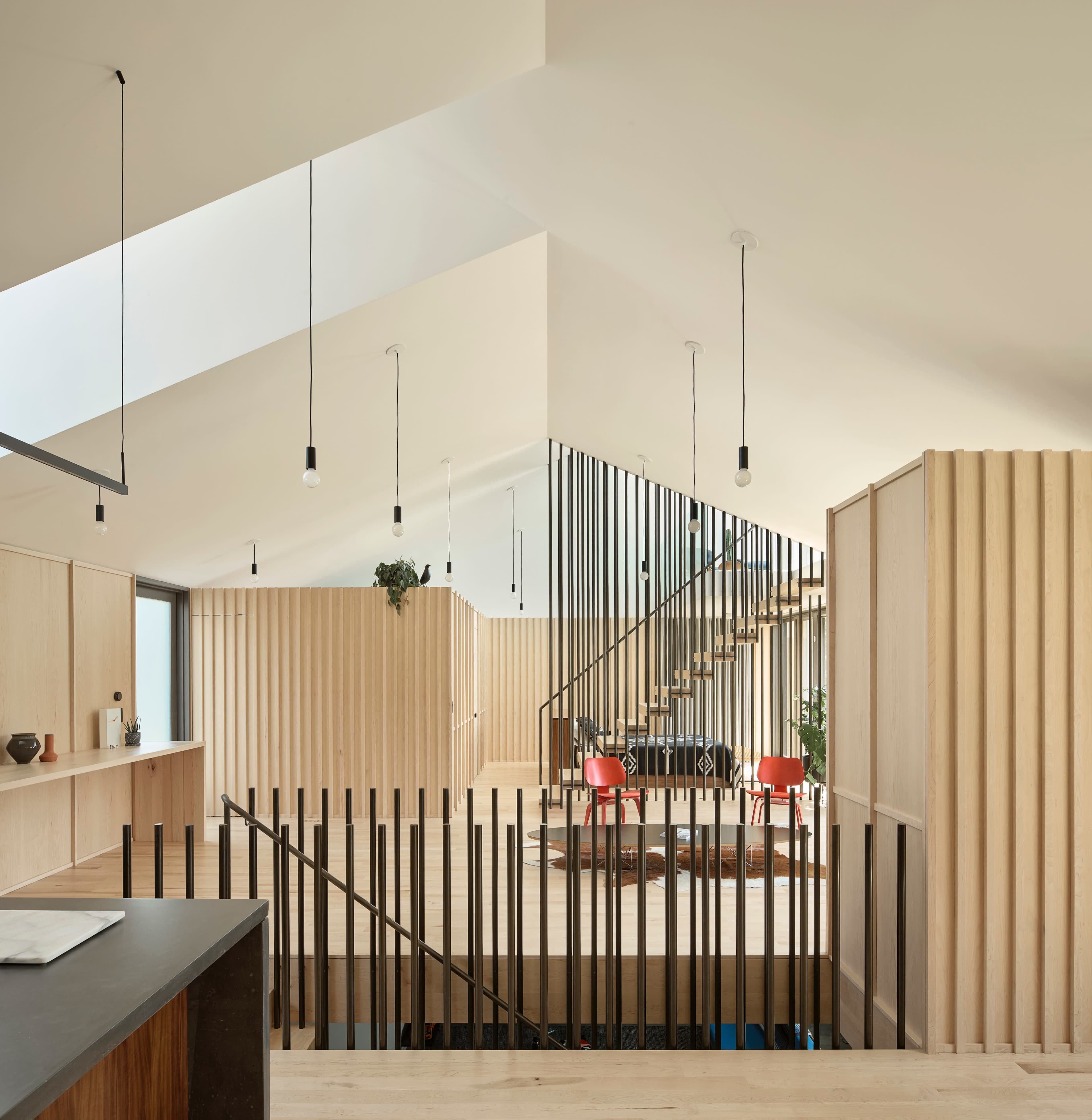 A modern interior space featuring wooden paneling, a staircase with black vertical slats, and a bright area with minimalist furnishings.