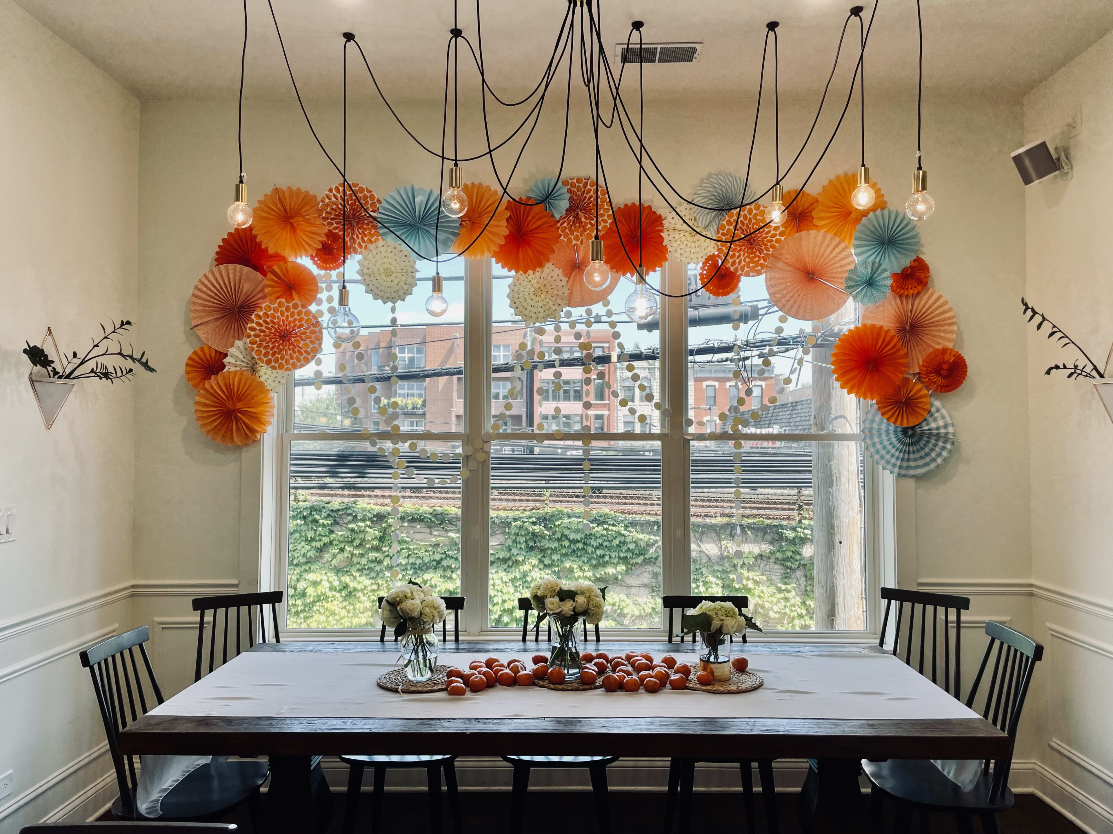 A dining room table with a bunch of paper umbrellas hanging from the ceiling for a gender neutral baby shower.