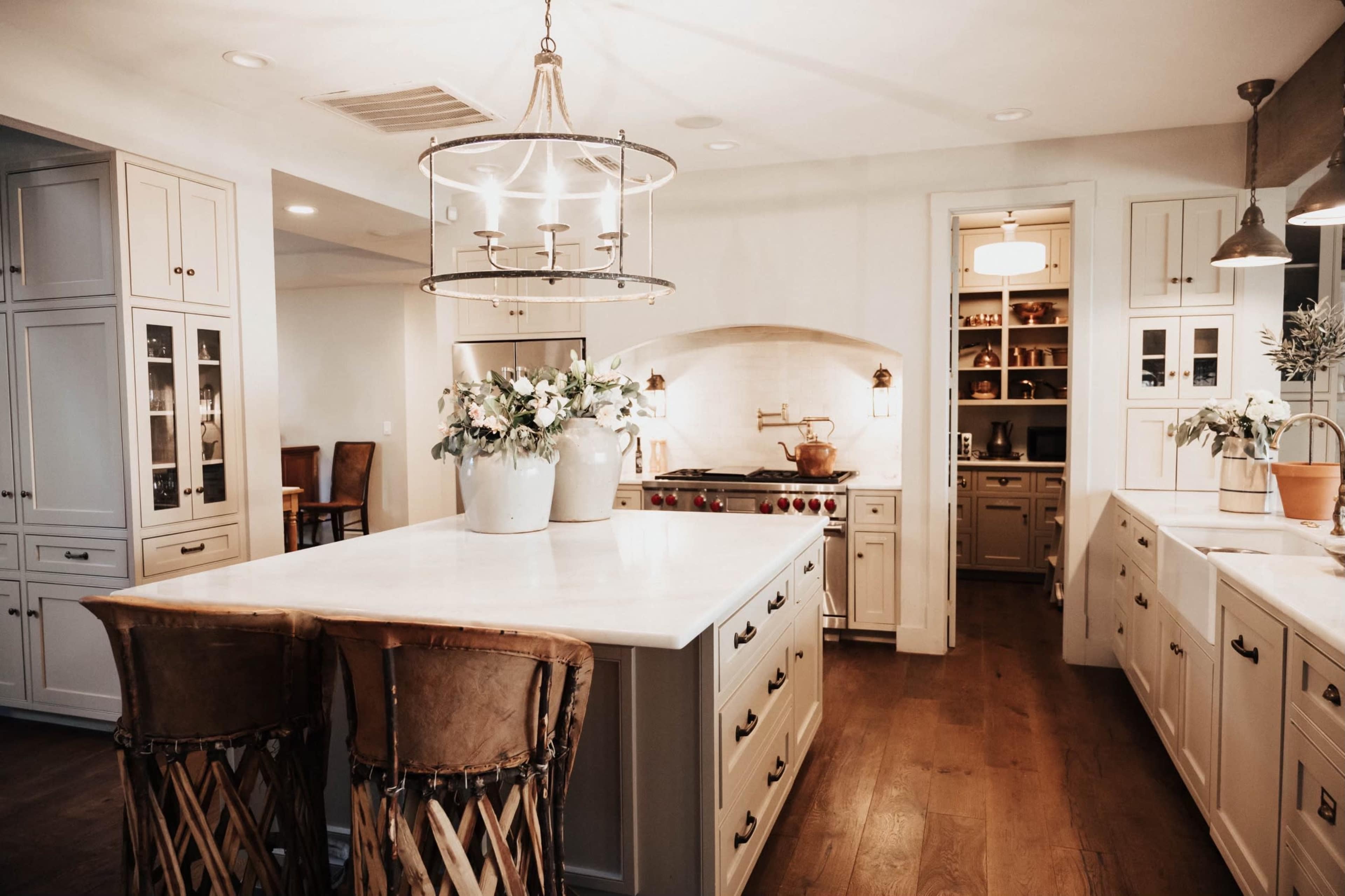 The kitchen features a central island with bar stools, white cabinetry, and a stove surrounded by a decorative arch.