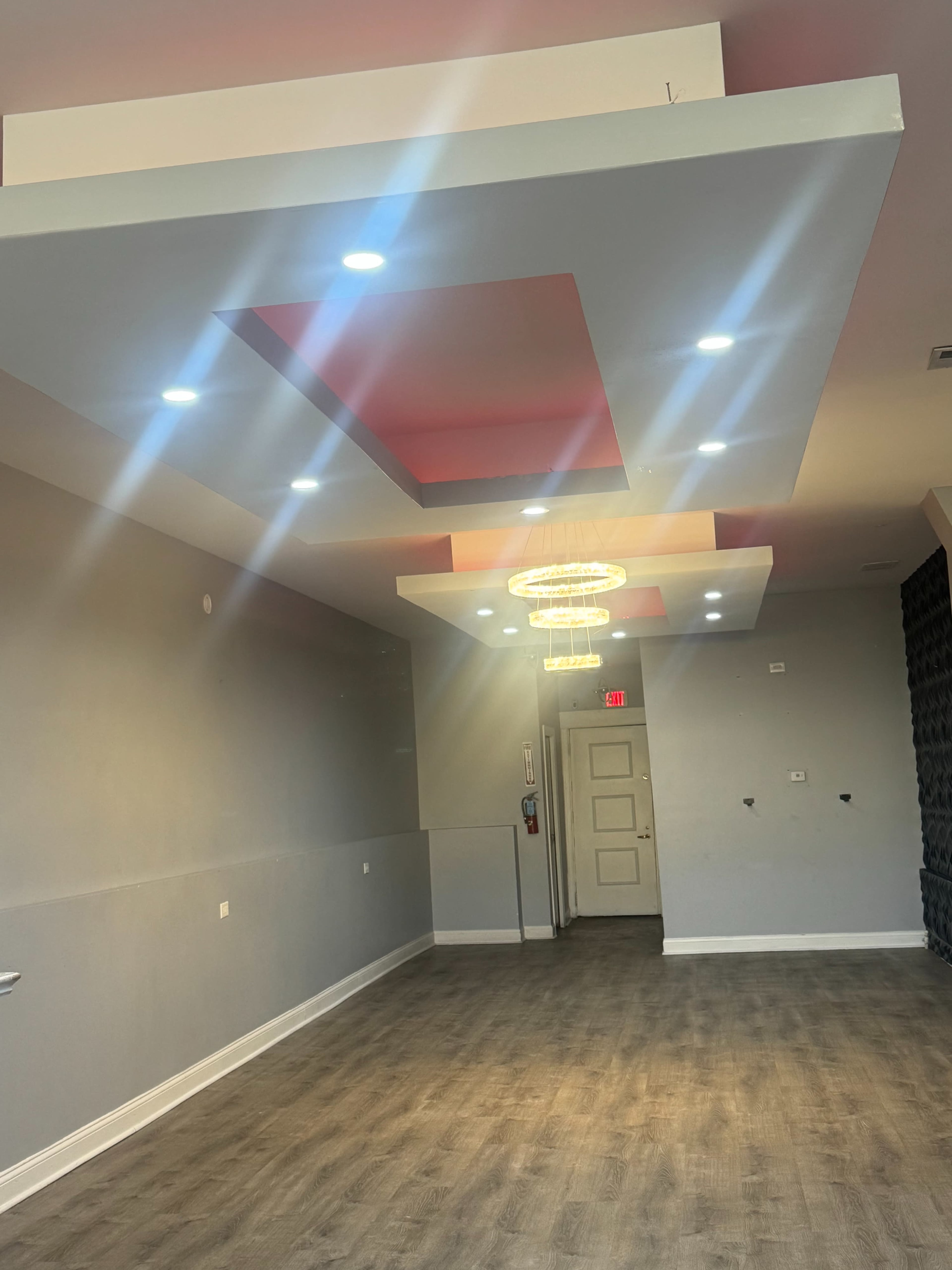 The image shows a well-lit empty interior space with a modern ceiling design and wooden flooring.