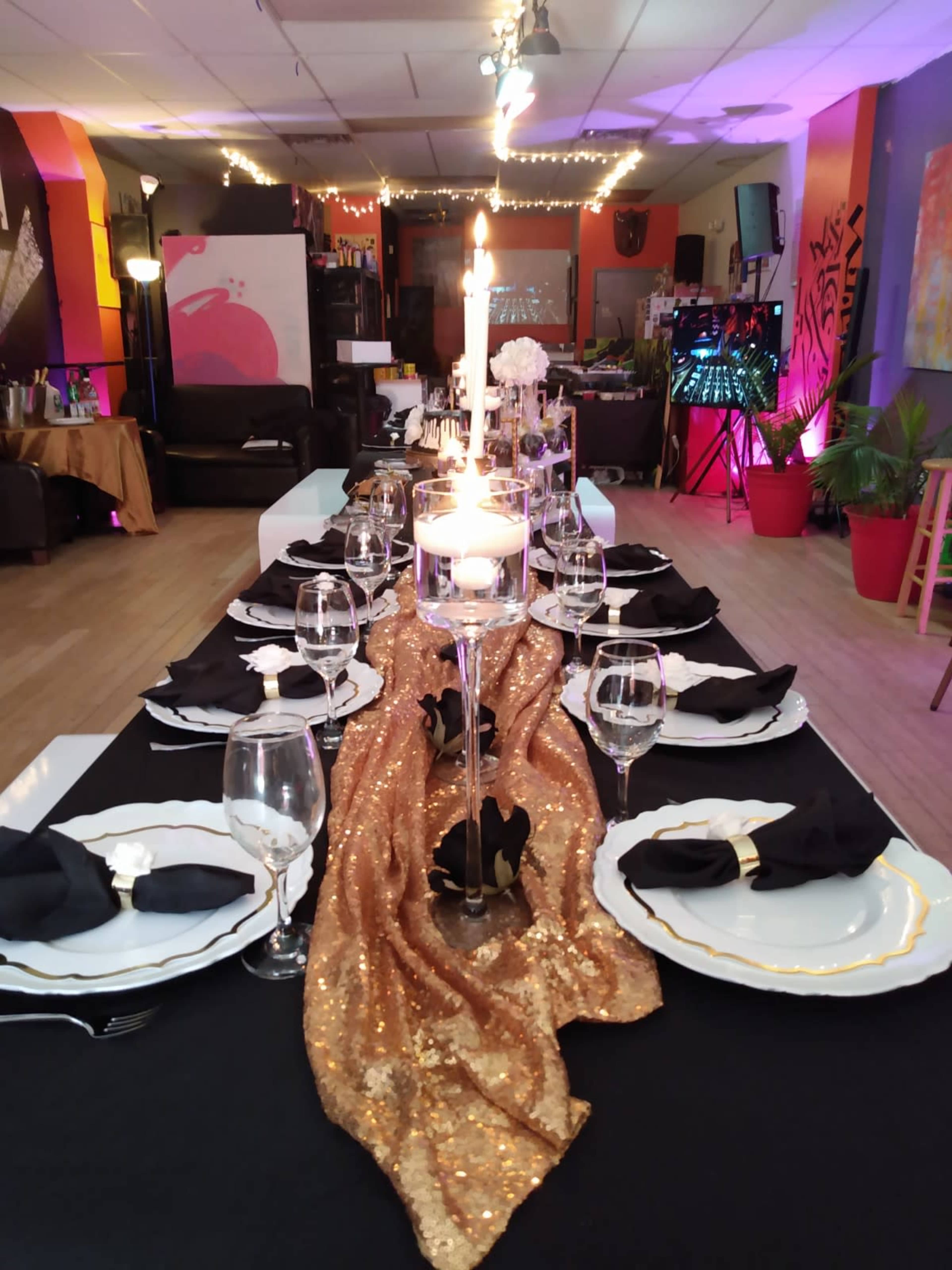 A long dining table is set with elegant place settings, a golden table runner, and a lit candle in the center.