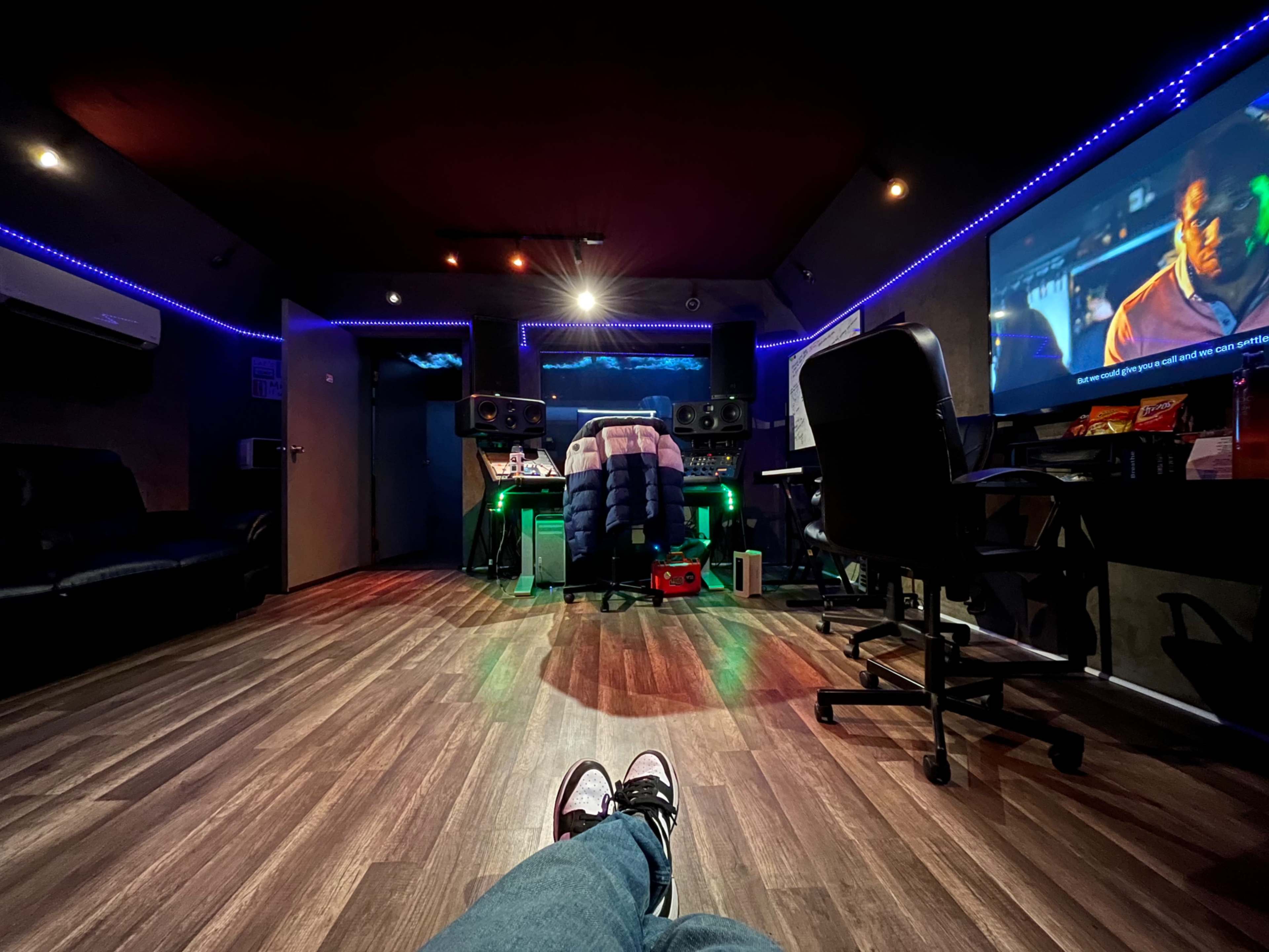 A music studio with a view of a large screen displaying a film, surrounded by audio equipment and seating areas.