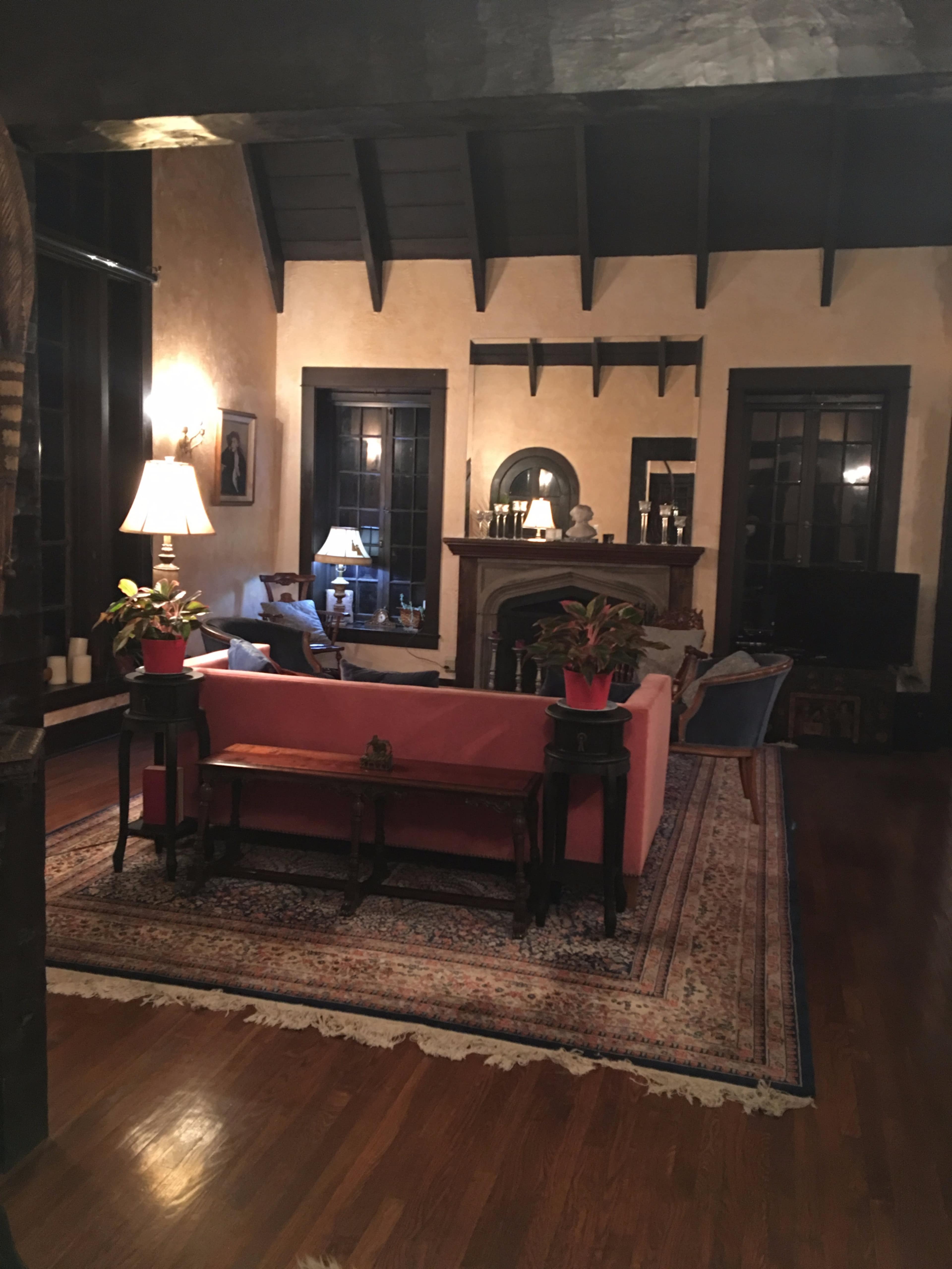 A cozy living room features a pink sofa, a decorative rug, and large windows with dark trim, illuminated by warm lamp light.