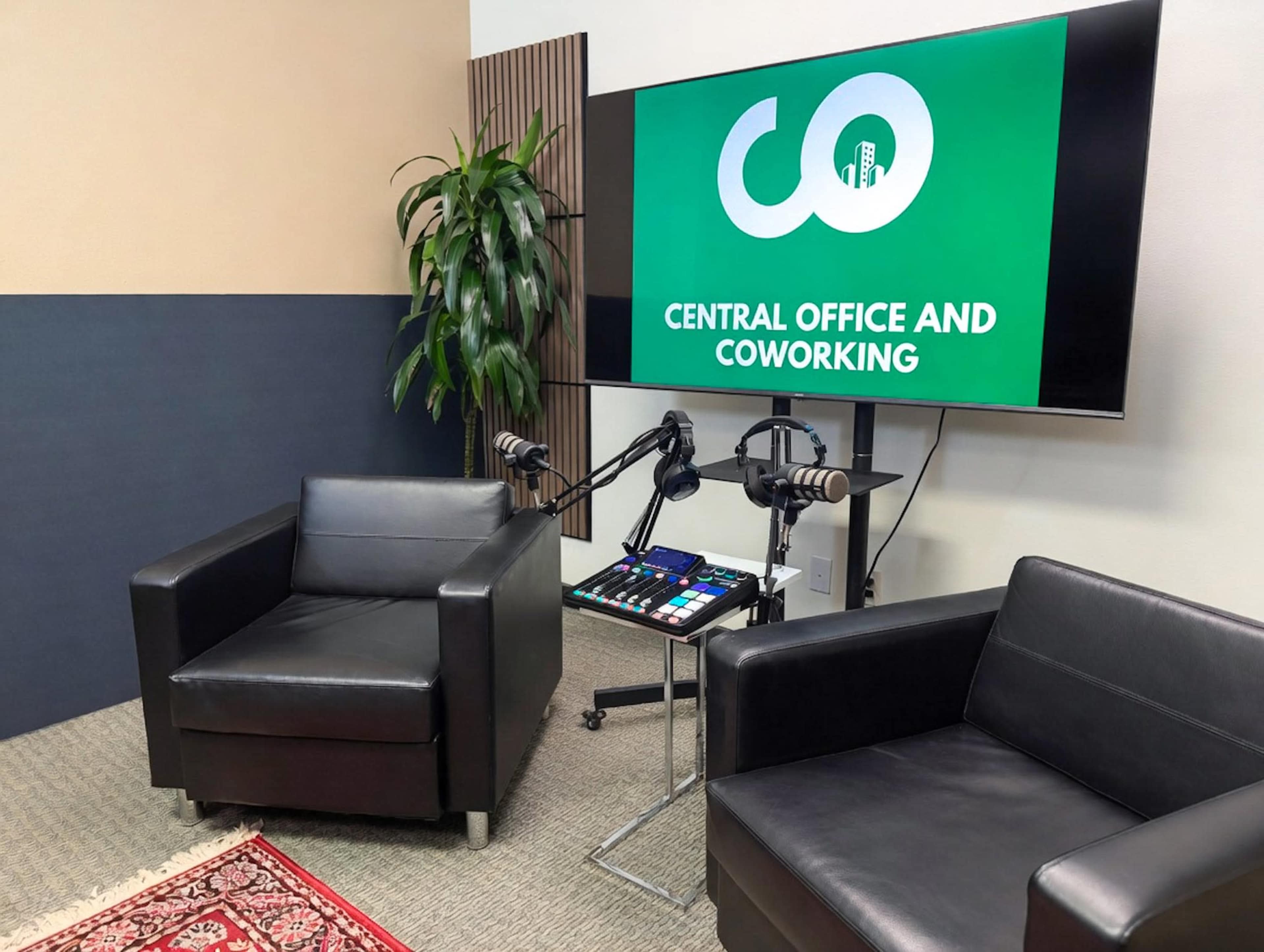 The image shows a modern coworking space with two black armchairs, a green wall display that reads "CENTRAL OFFICE AND COWORKING," and audio equipment set up on a small table.