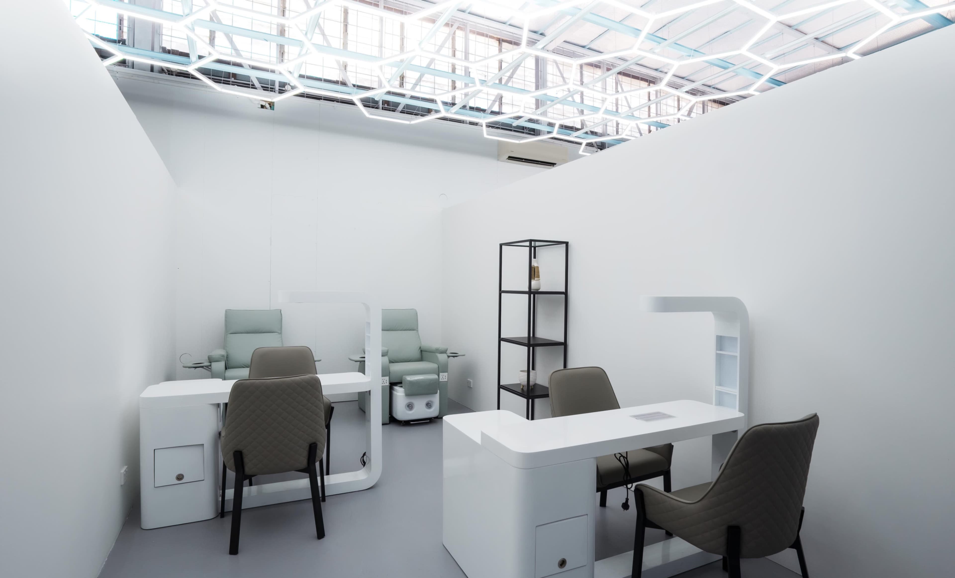 The image shows a minimalist office space with two workstations, each equipped with a chair and a desk, and a small shelving unit in the corner.