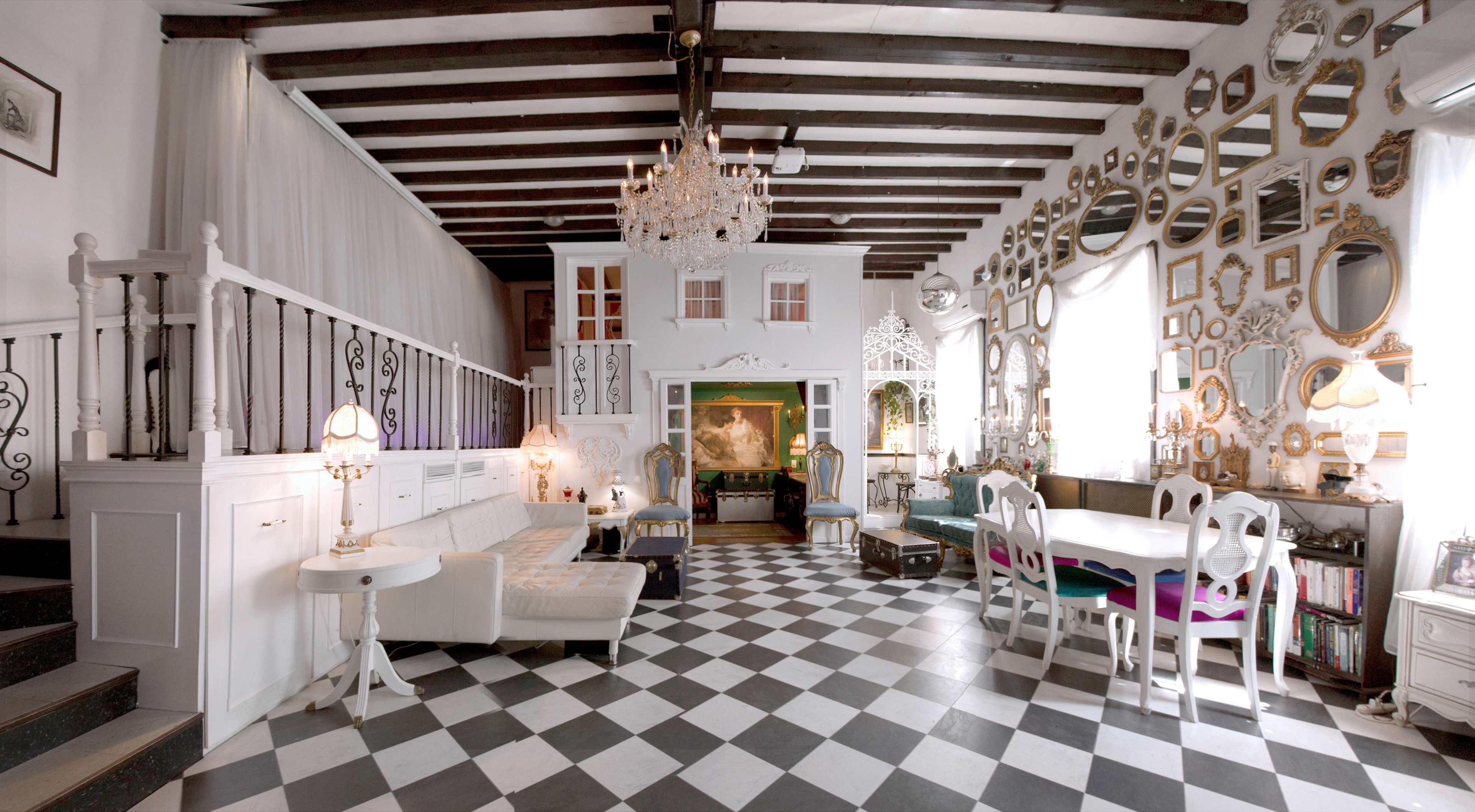A spacious room with a checkered black and white floor, featuring a white seating area, a dining table, and numerous mirrors arranged on the walls.