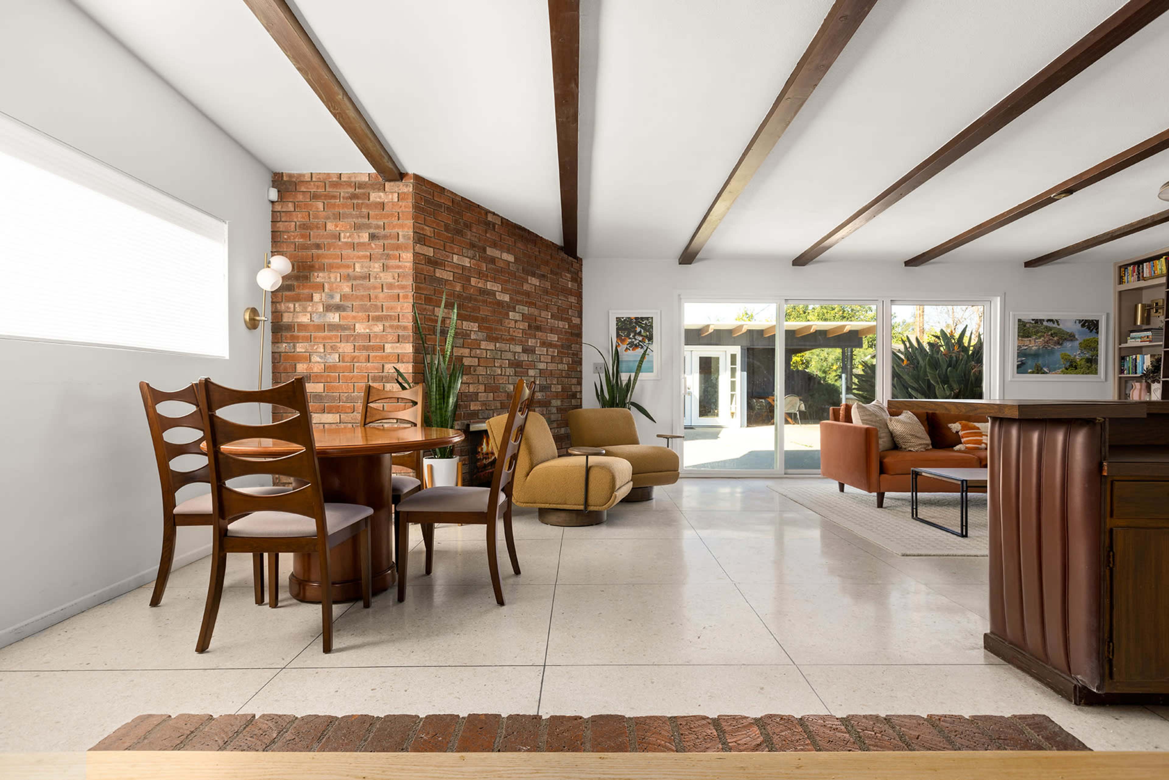 A modern living space featuring a dining area with a wooden table and chairs, a sectional sofa, and large windows that allow natural light to enter.