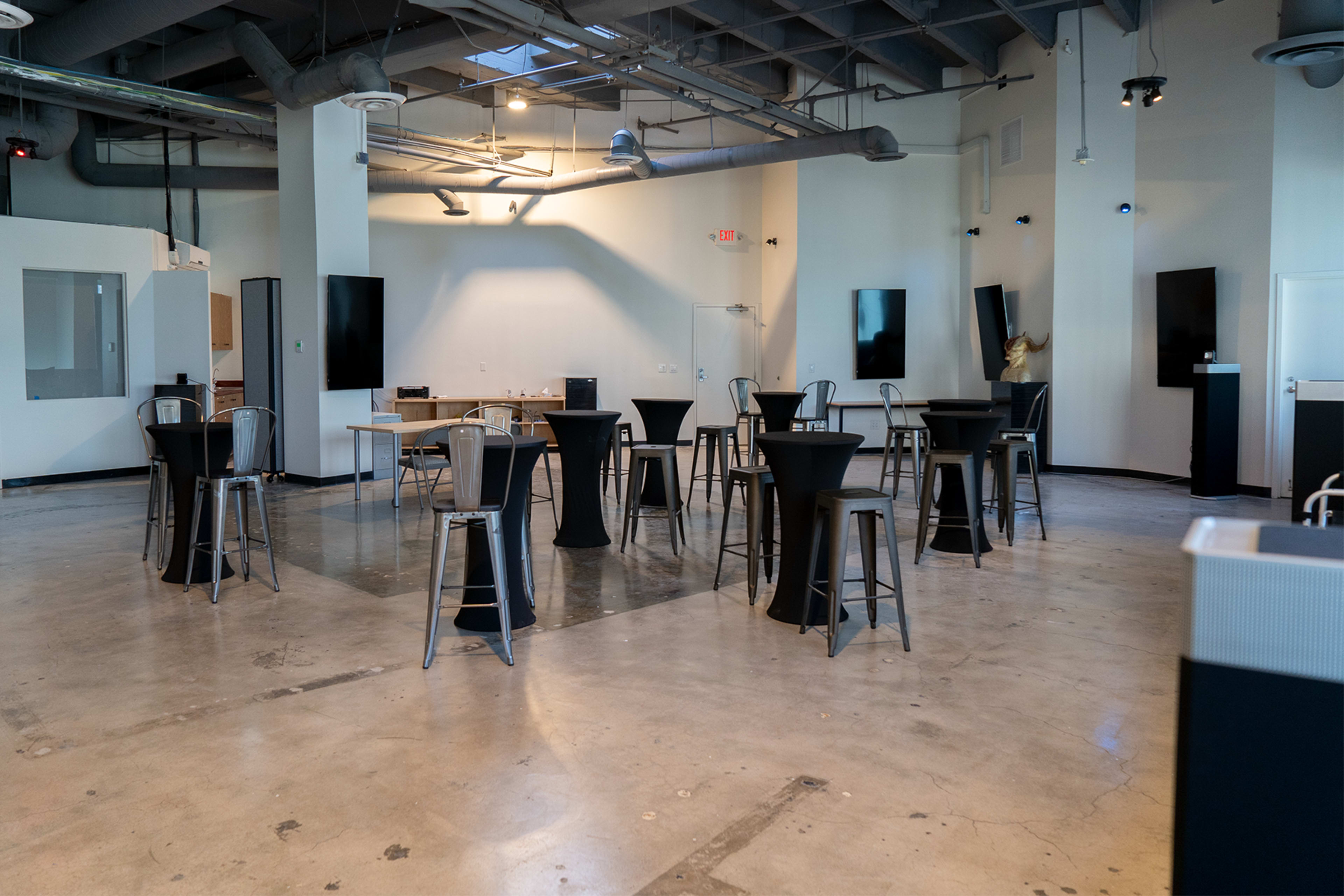 An empty, modern event space with high tables and bar stools arranged in a circle on a concrete floor.