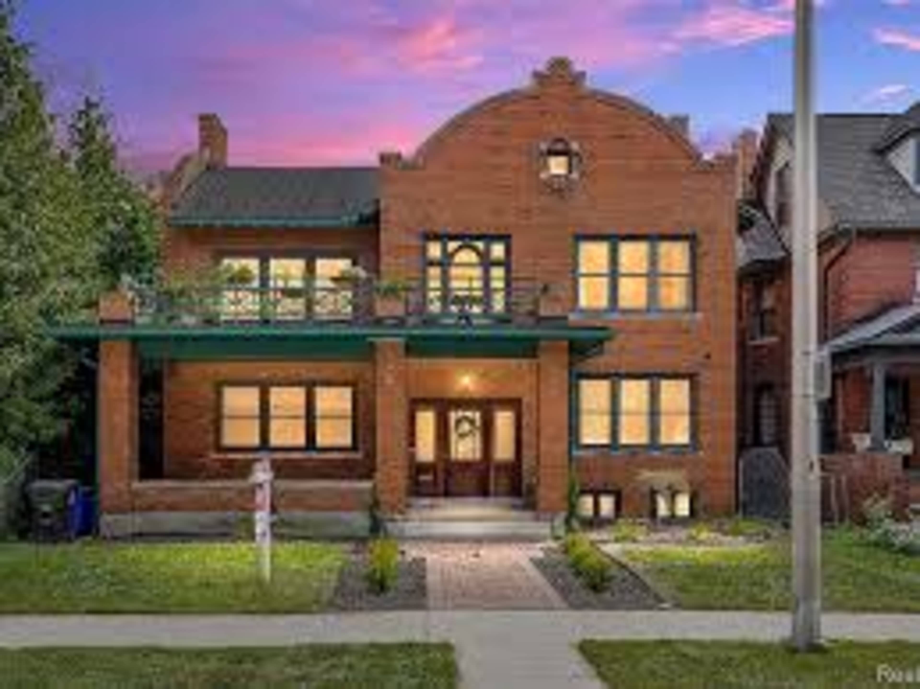 The image shows a large, two-story brick house with a decorative facade and several windows set against a twilight sky.