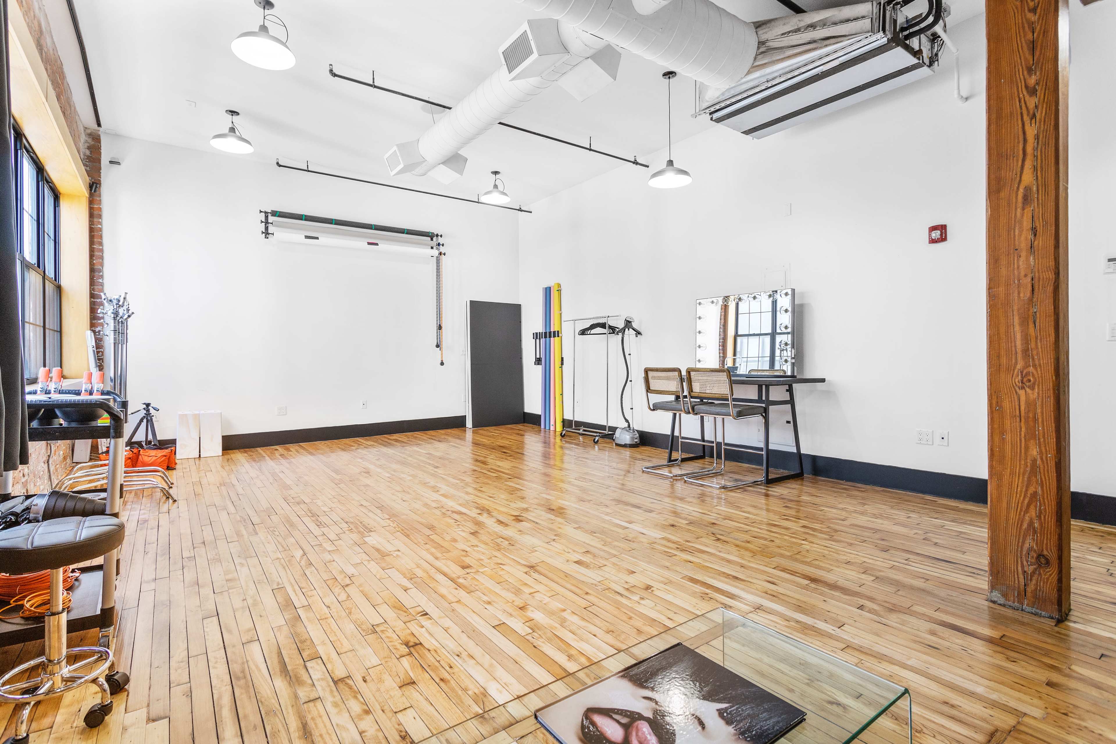 A spacious, well-lit studio with wooden floors, a large mirror, and two chairs, featuring minimalist decor and industrial elements.