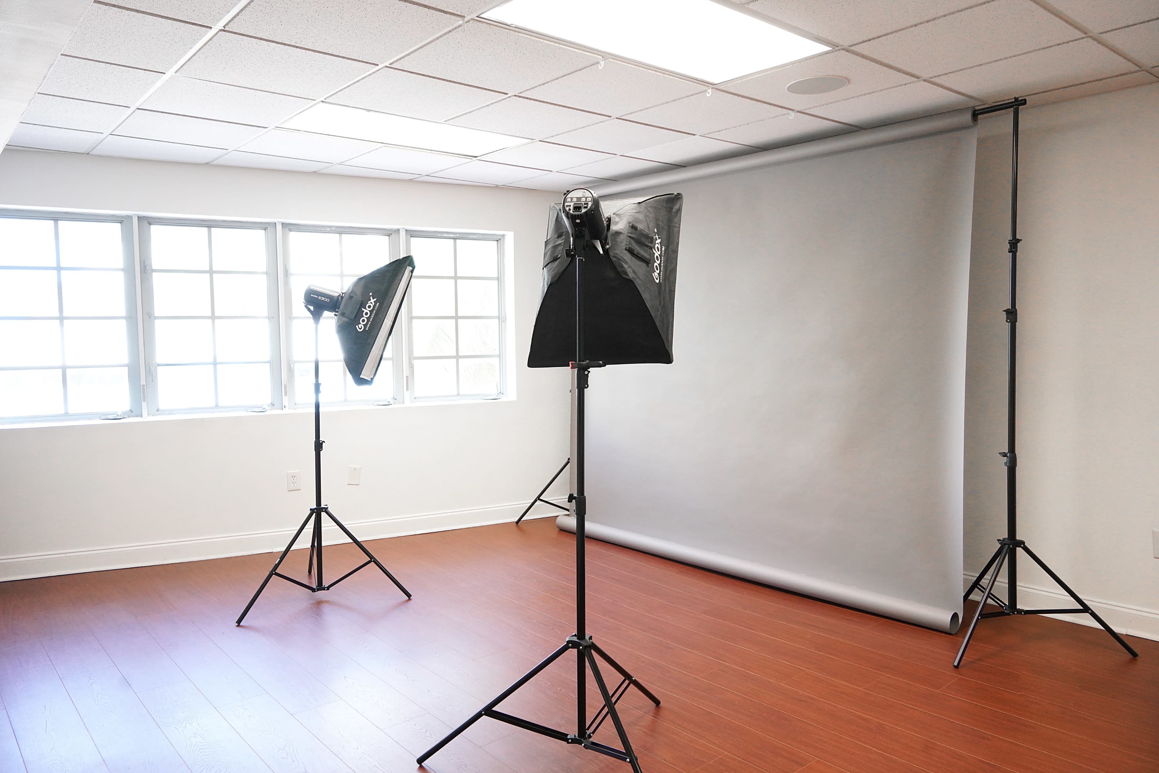 A photography studio with two softbox lights positioned on stands and a gray backdrop set up against the wall.
