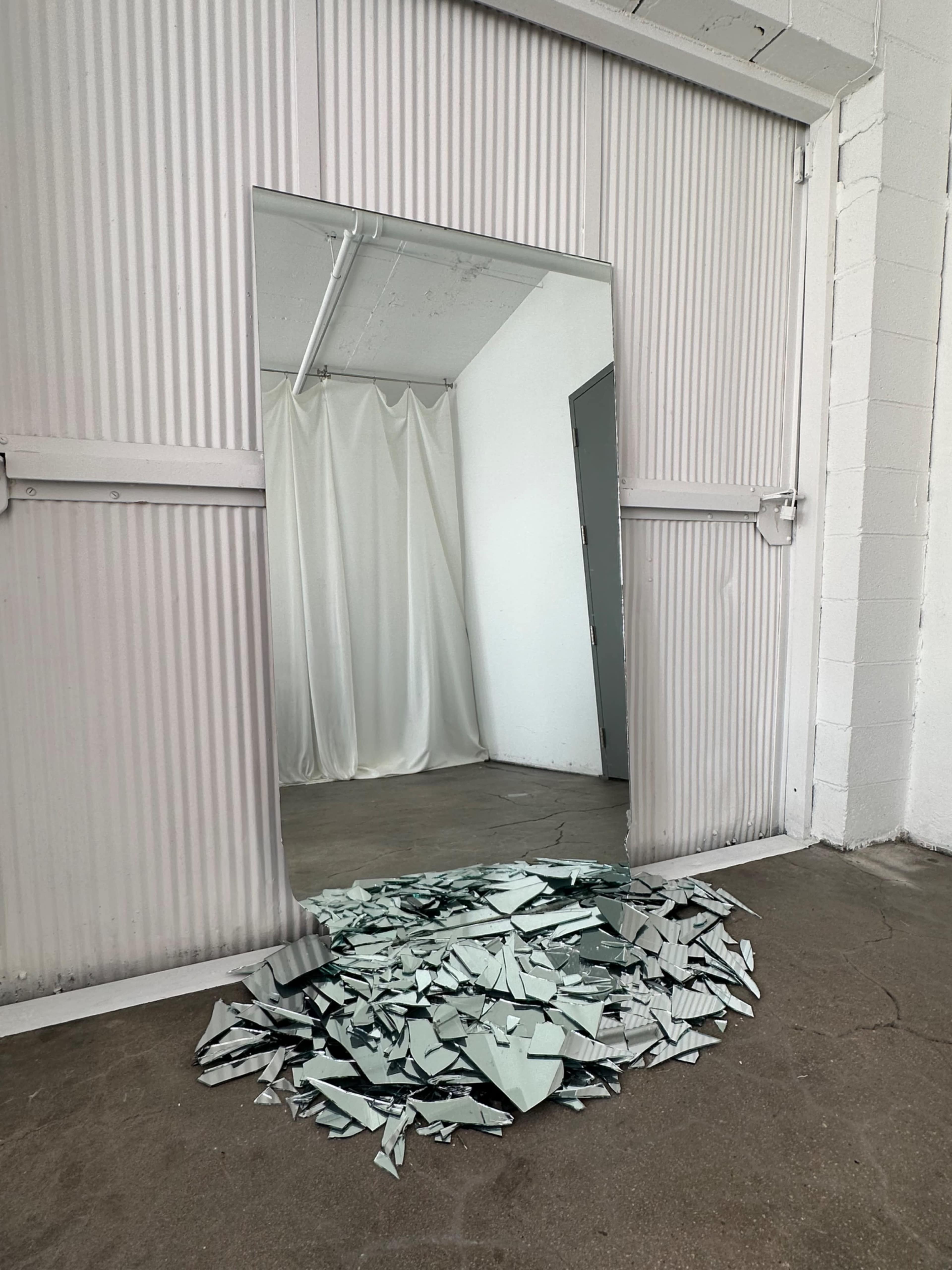 A doorway with a mirrored frame leads into a room, where a pile of shattered mirror pieces is scattered on the floor.