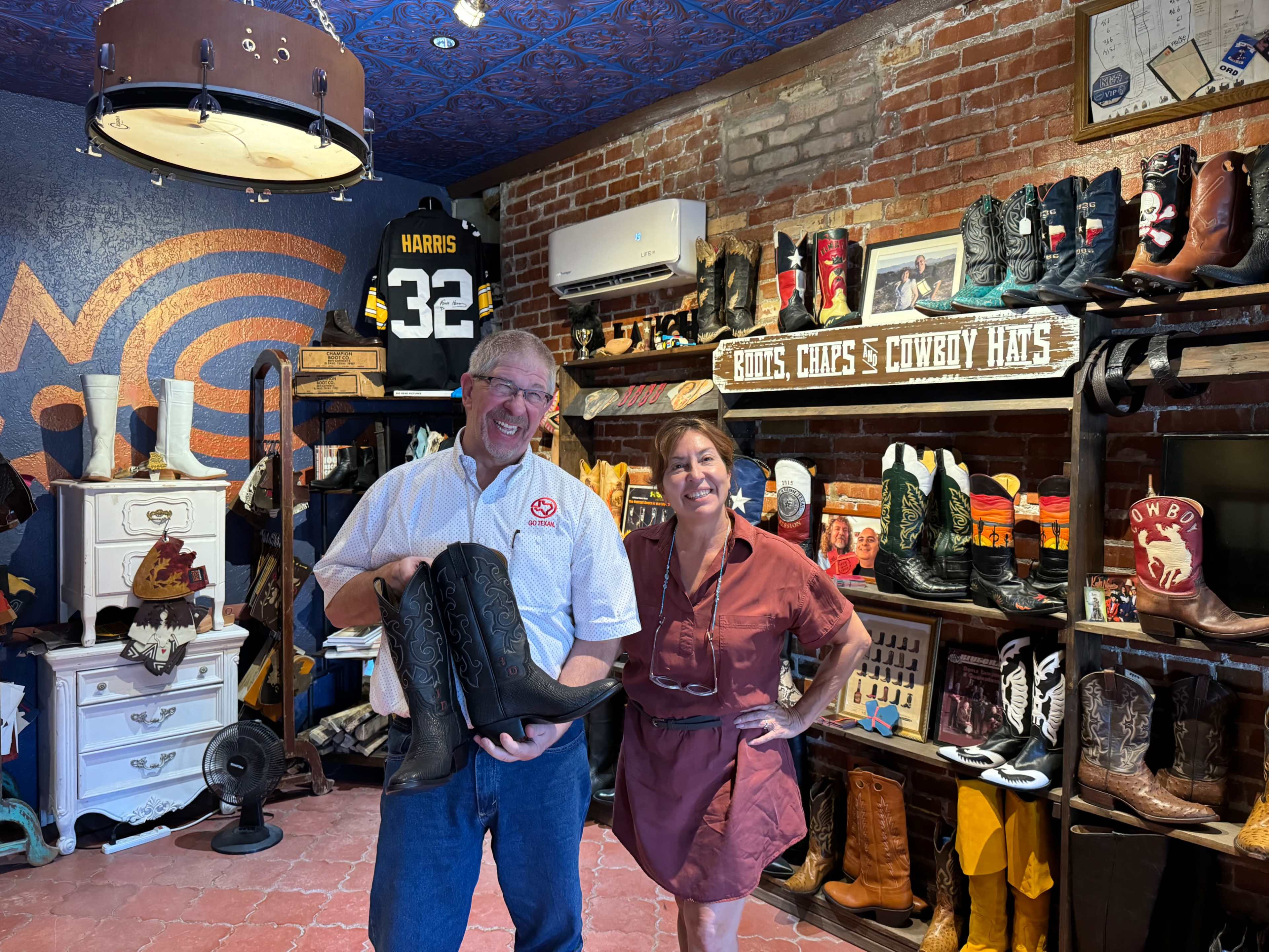 A man and a woman pose together in a store filled with cowboy boots and hats, with various merchandise displayed on shelves and walls.