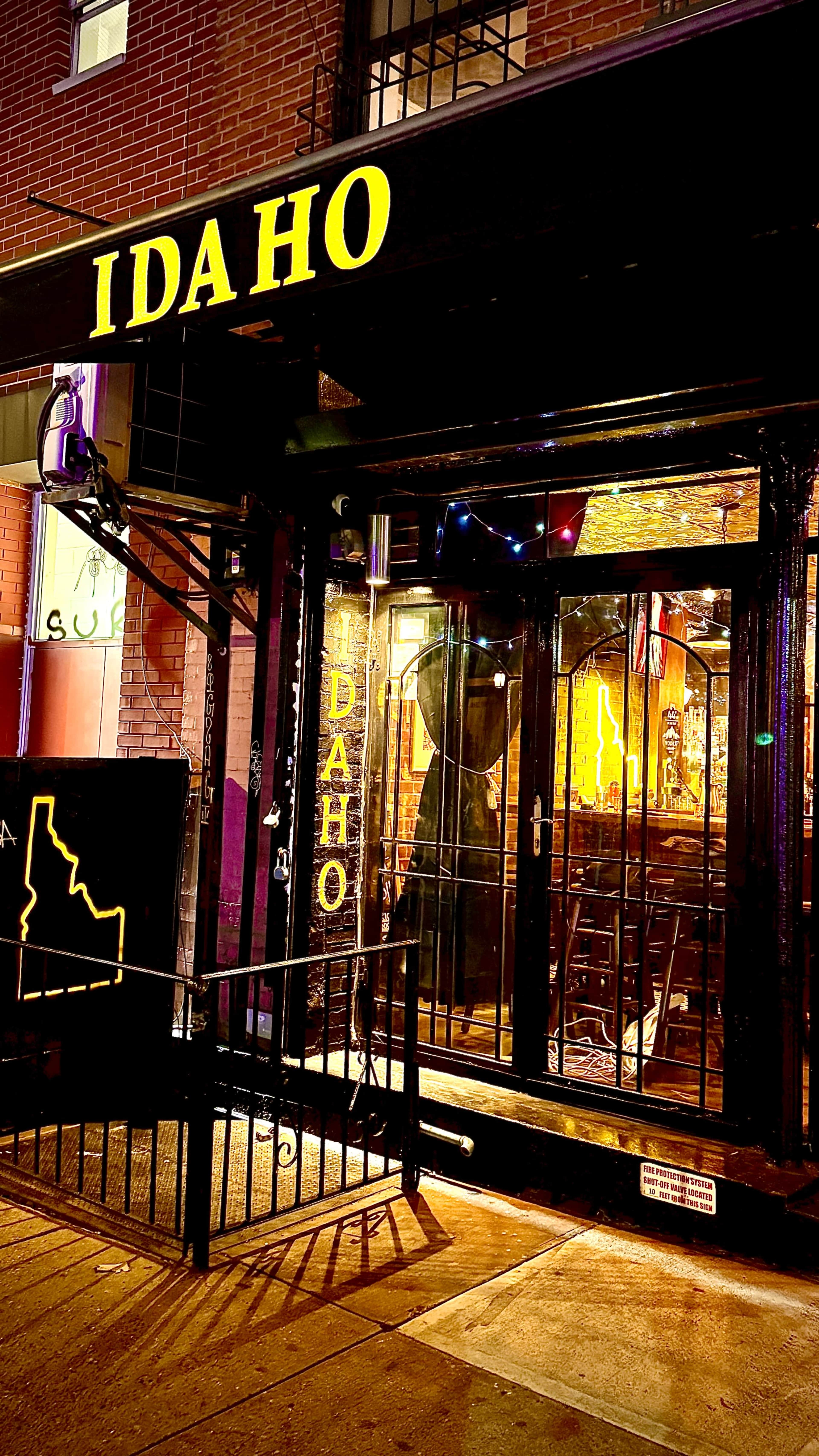 The photo shows a restaurant entrance with a yellow sign that reads "IDAHO" and a stylized outline of the state of Idaho on a black board outside.