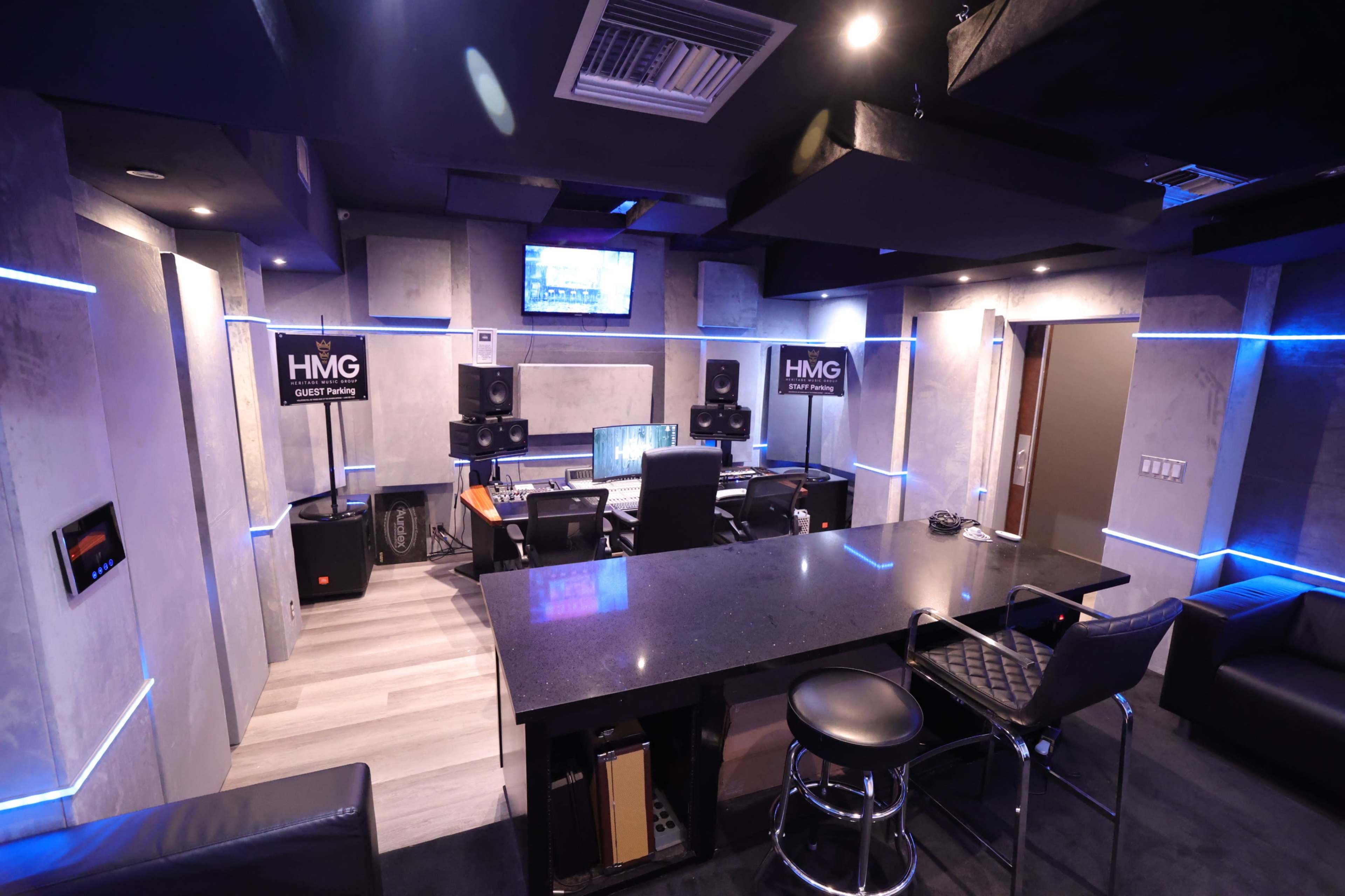 The image shows a modern music studio with sound equipment, a mixing desk, and a sleek black countertop surrounded by acoustic wall panels.