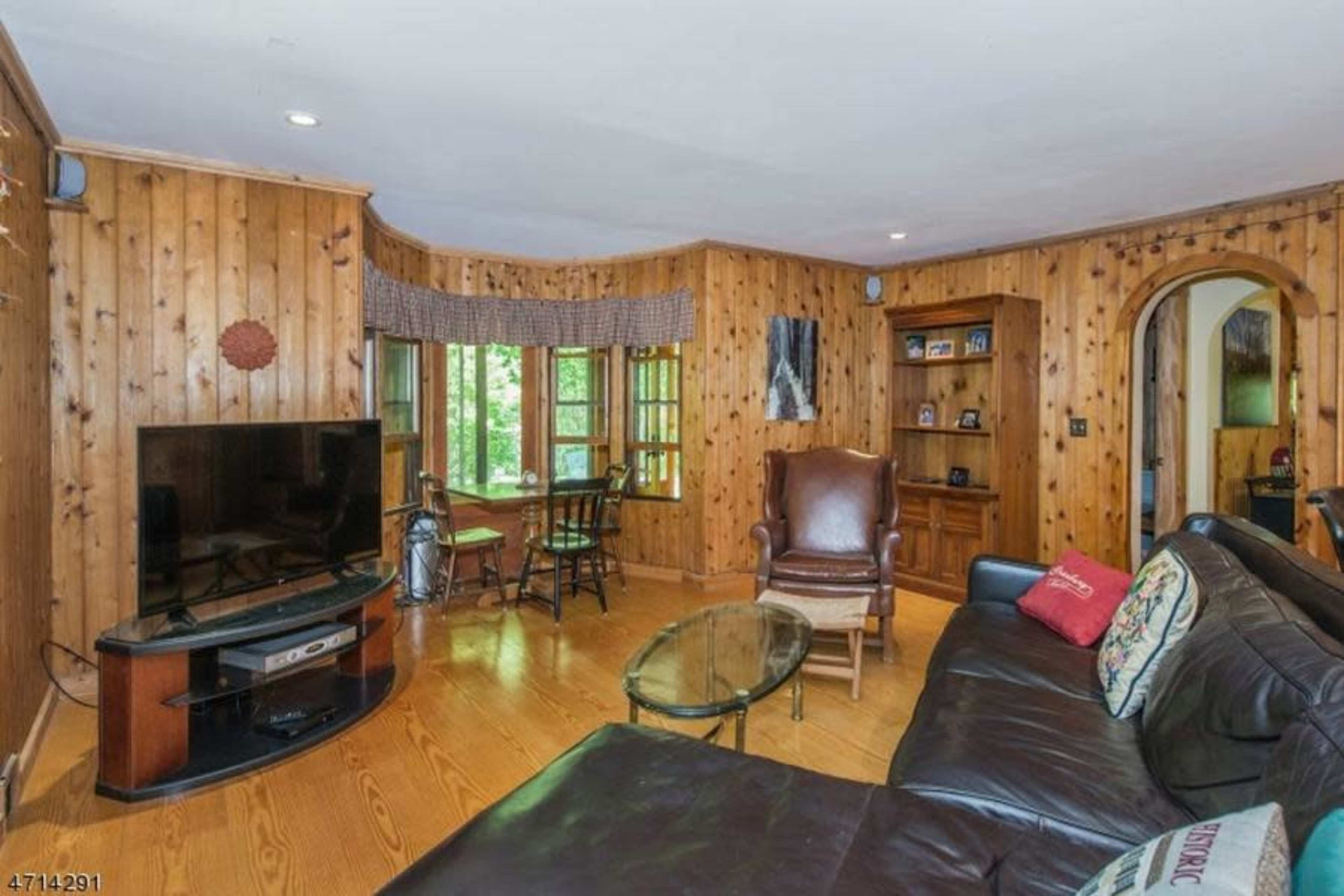 A wooden-paneled living room featuring a leather sofa, a coffee table, a television, and large windows letting in natural light.