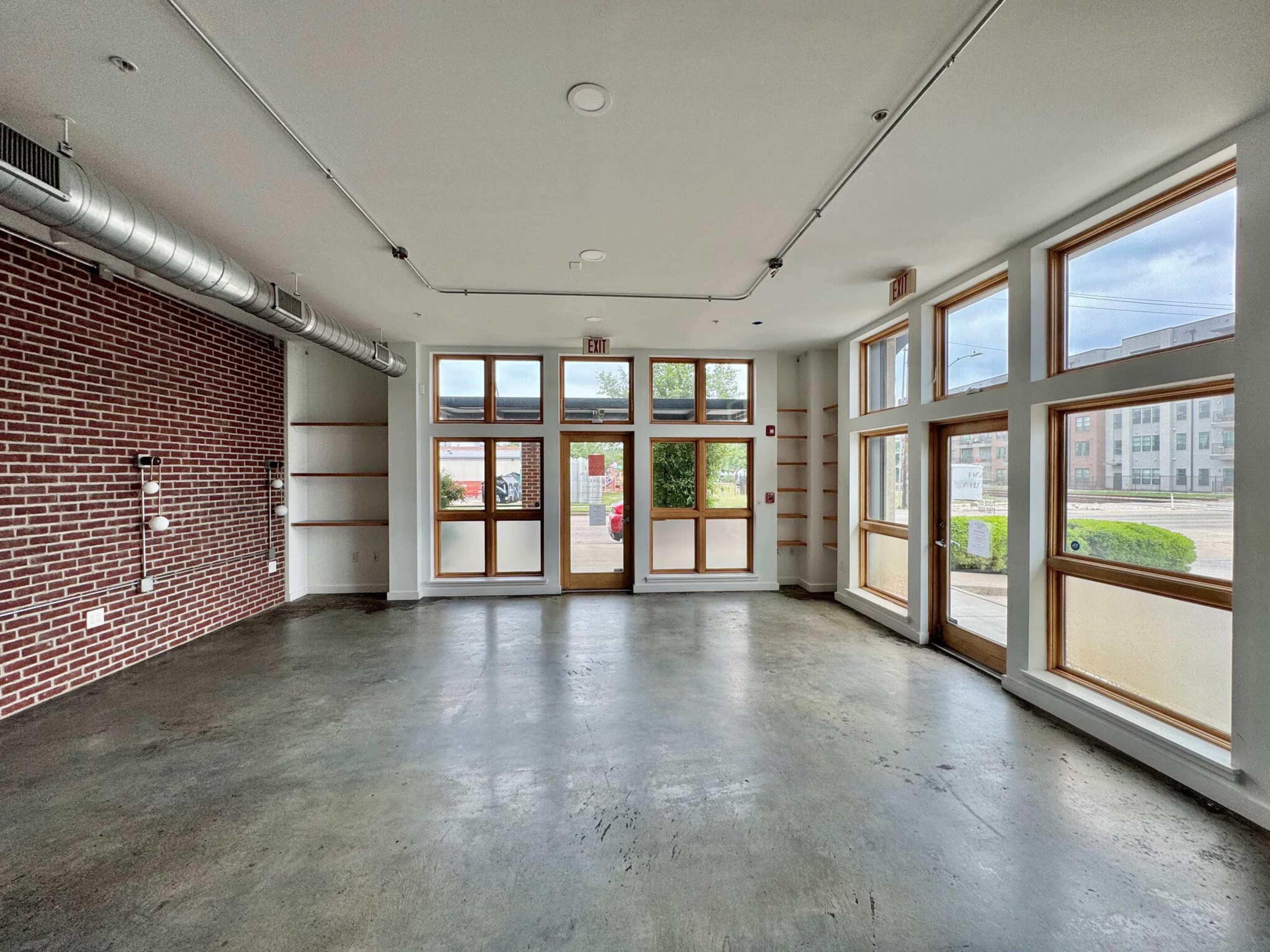 The image shows an empty commercial interior space with large windows and a brick wall.