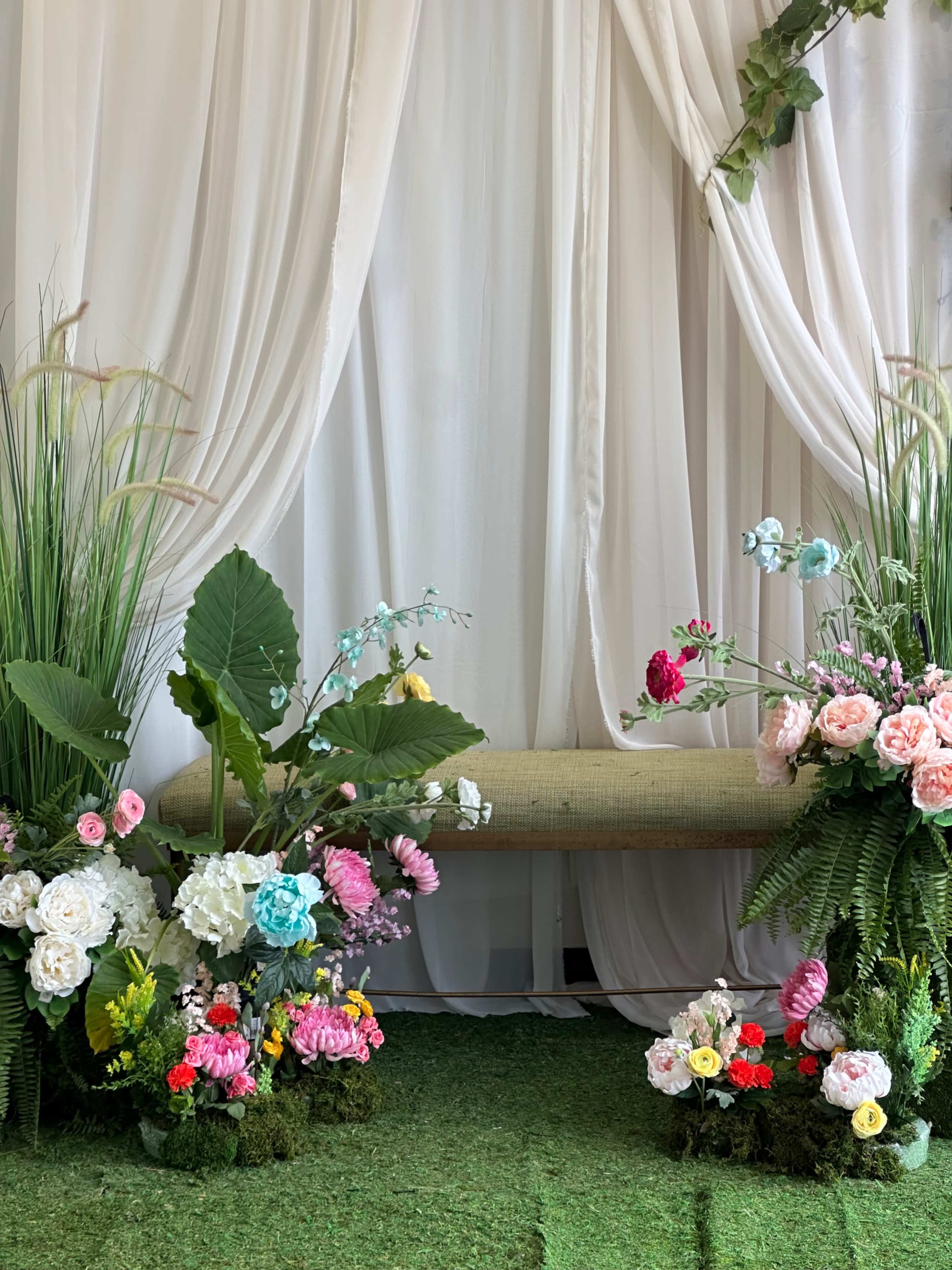 A decorative backdrop features a bench surrounded by various artificial flowers and greenery.