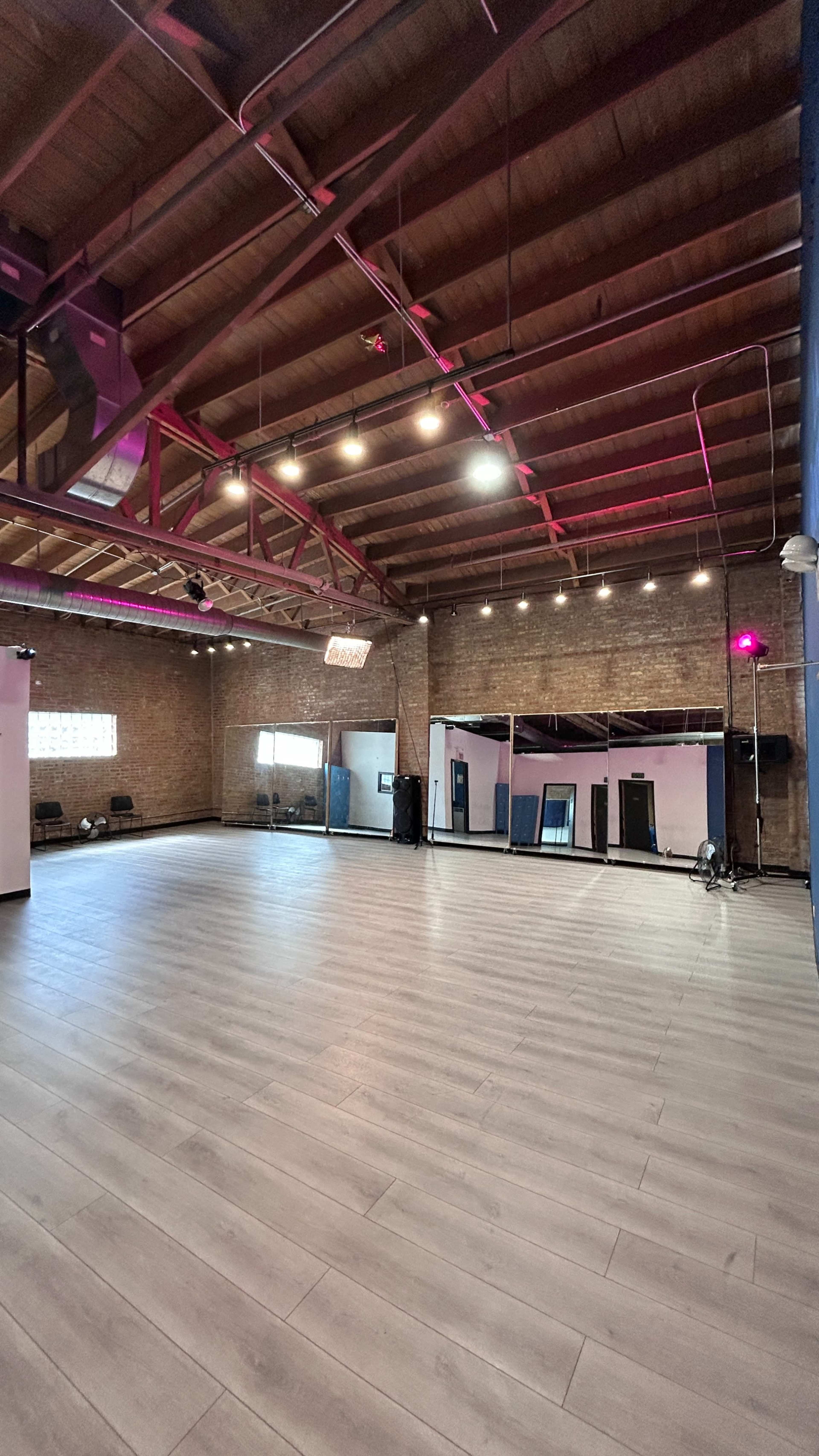 The image shows an empty, spacious interior of a dance or performance studio with wooden beams and large mirrors on the walls.