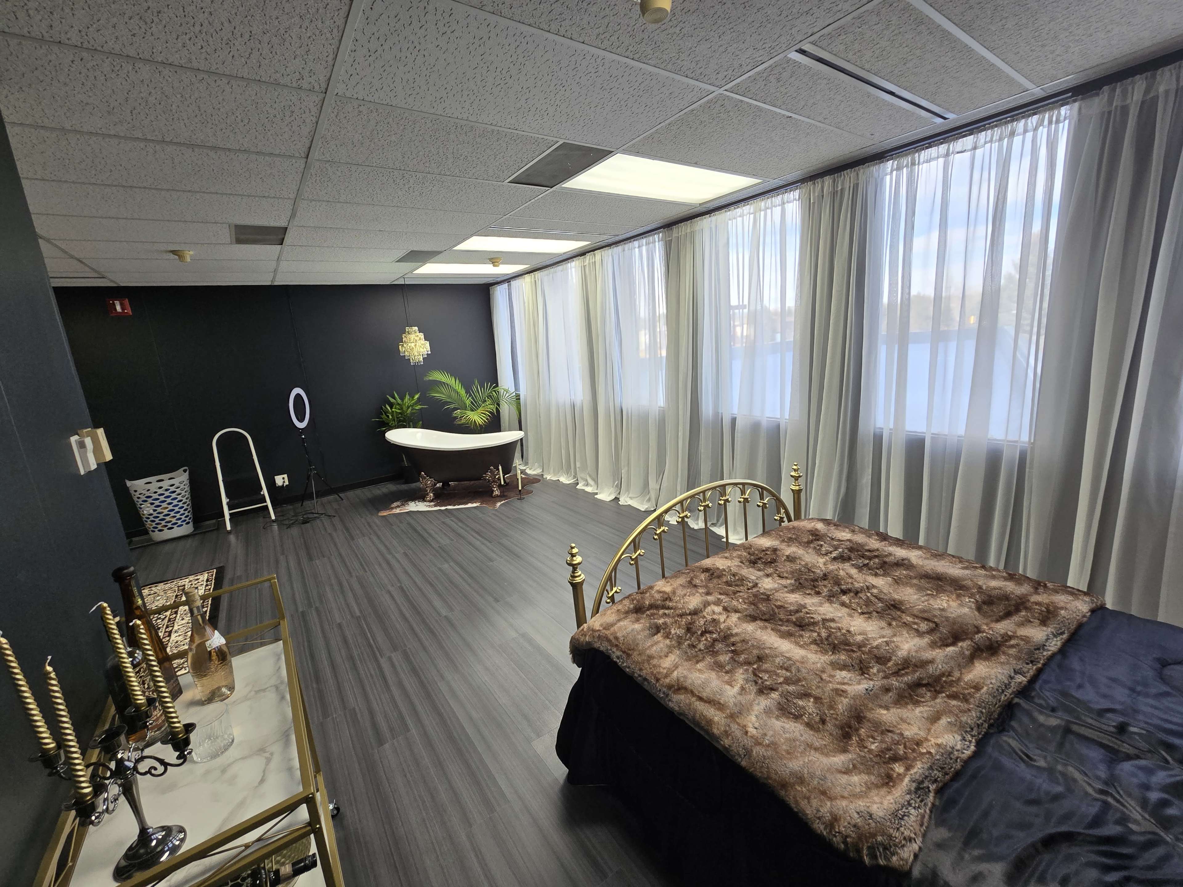 A modern room featuring a bed with a fur throw, a freestanding bathtub, large windows with sheer curtains, and a minimalist decor style.