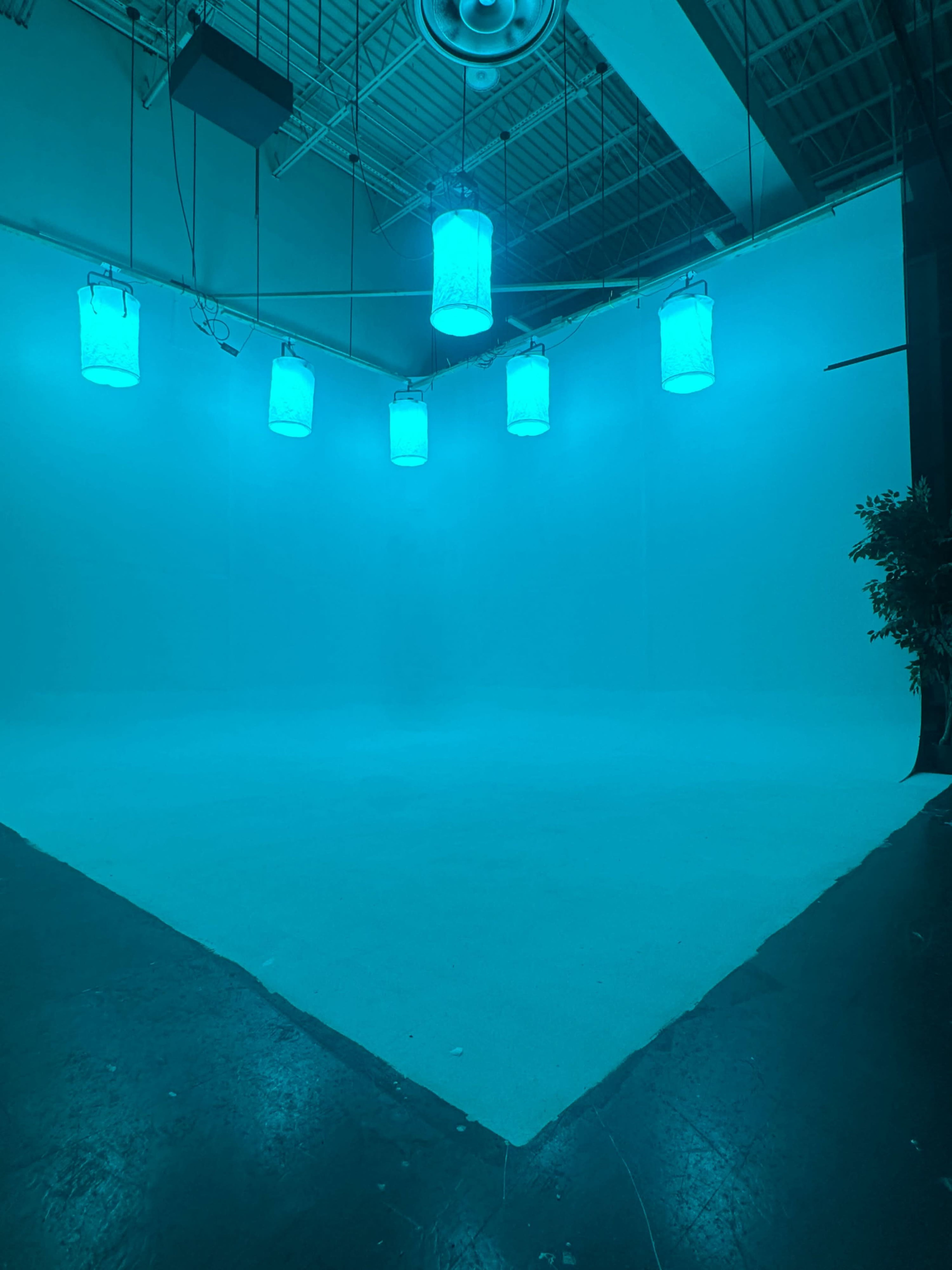 A spacious room with a blank, illuminated backdrop and several hanging lanterns emitting a blue light.