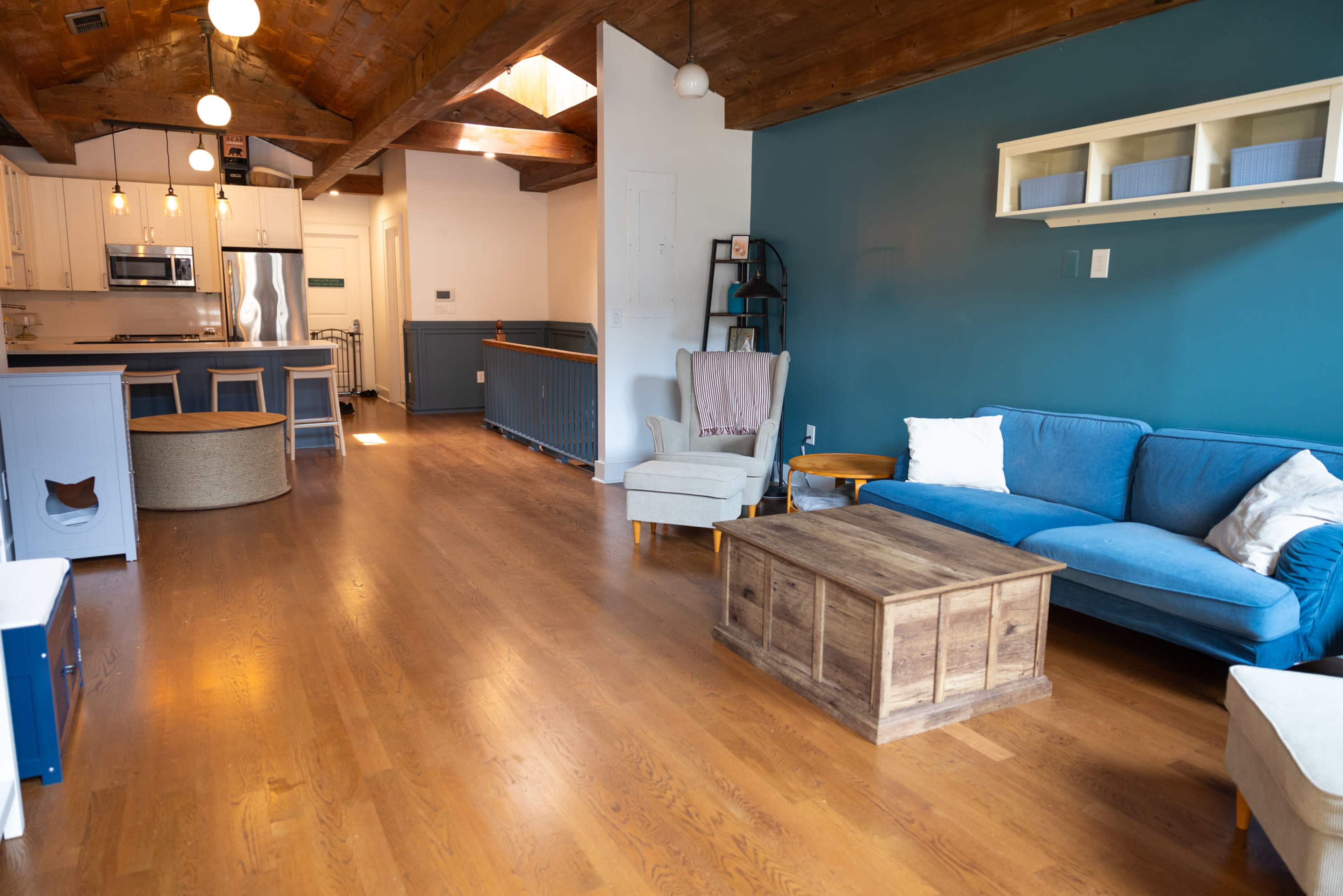 A spacious living area featuring a blue couch, a wooden coffee table, and an open kitchen area with white cabinetry and stainless steel appliances.