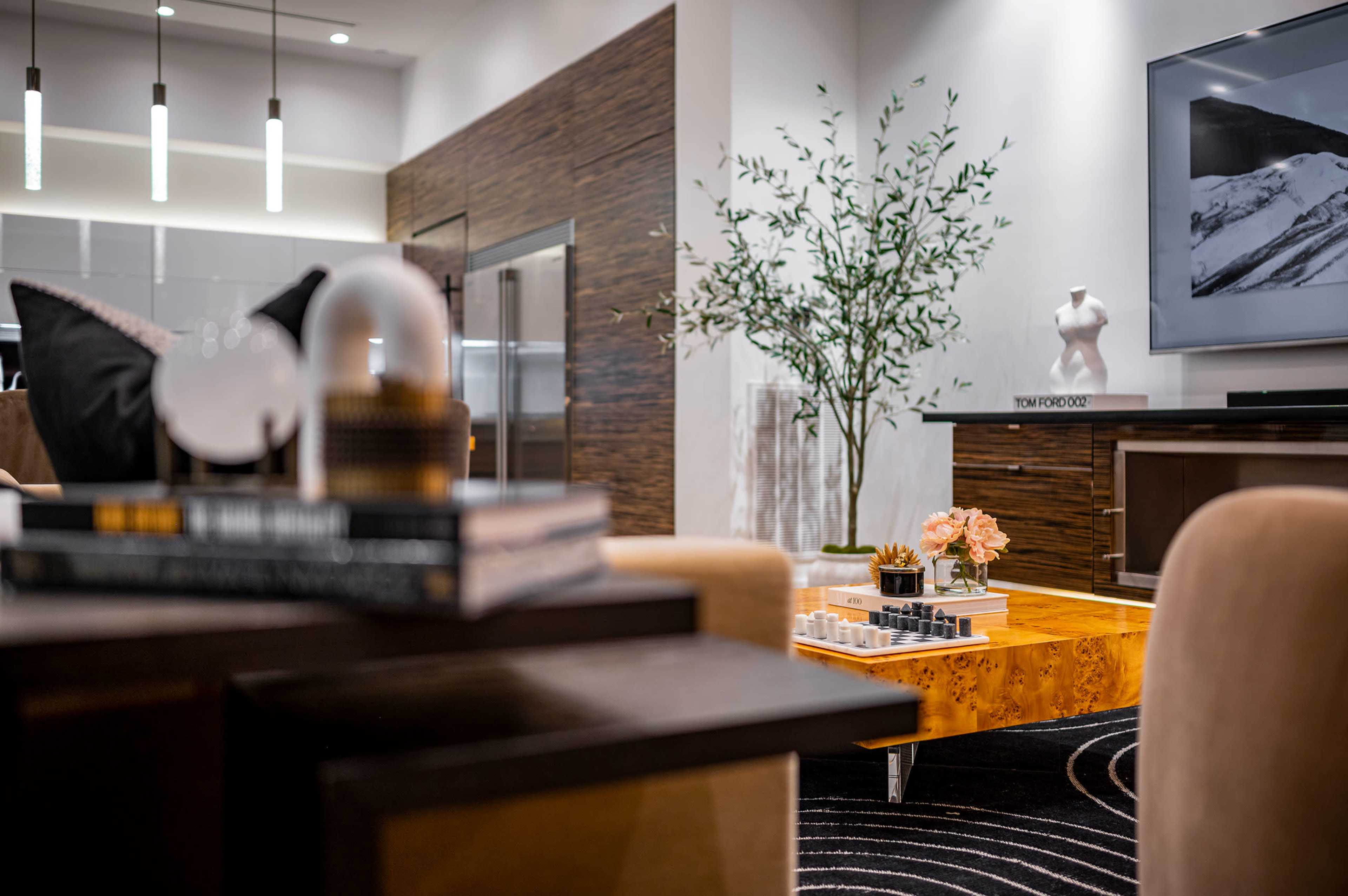 A modern living room with a coffee table, decorative plants, and a large television mounted on the wall.