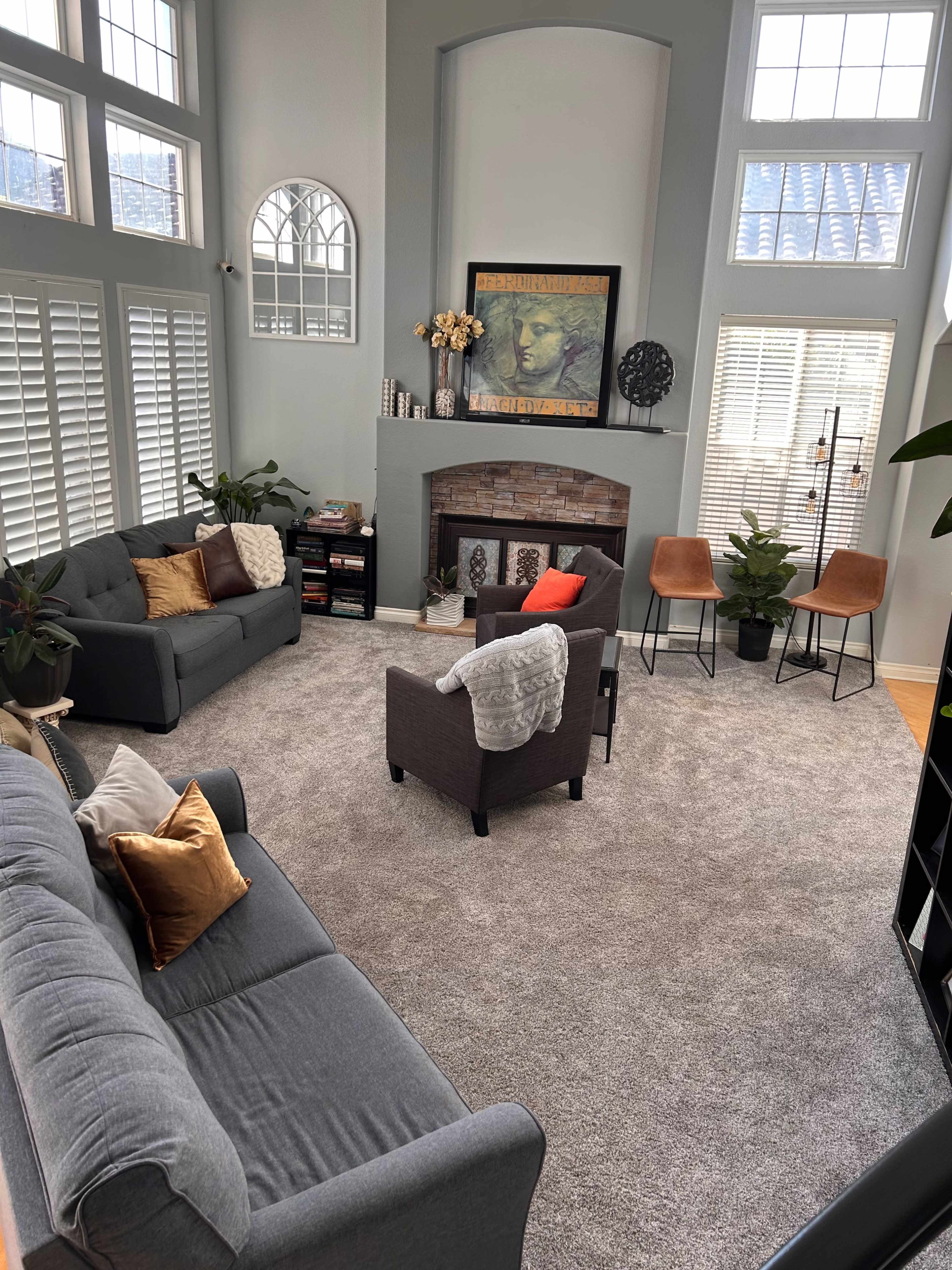 A spacious living room with two sofas, a fireplace, decorative plants, and large windows allowing natural light to fill the area.
