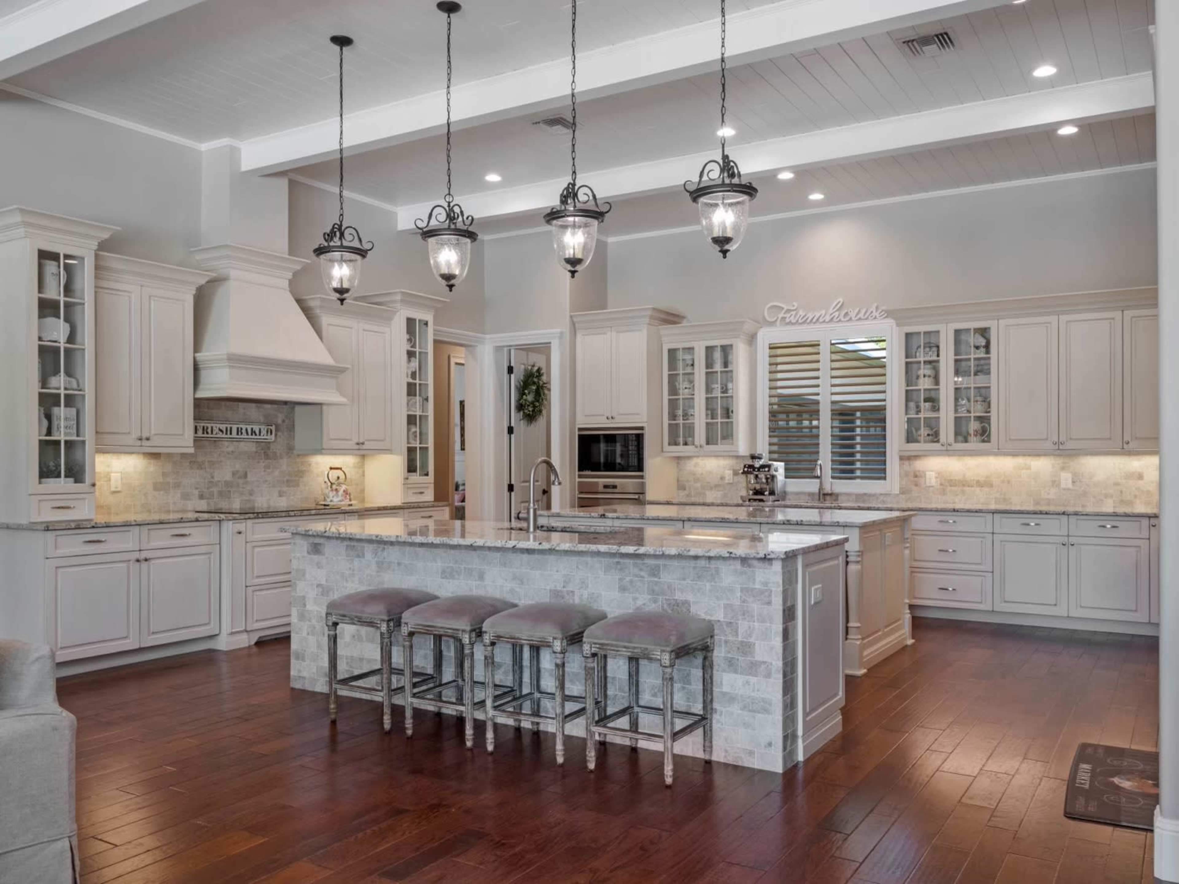 The image shows a modern kitchen with white cabinetry, a central island topped with gray stone, and pendant lighting above.