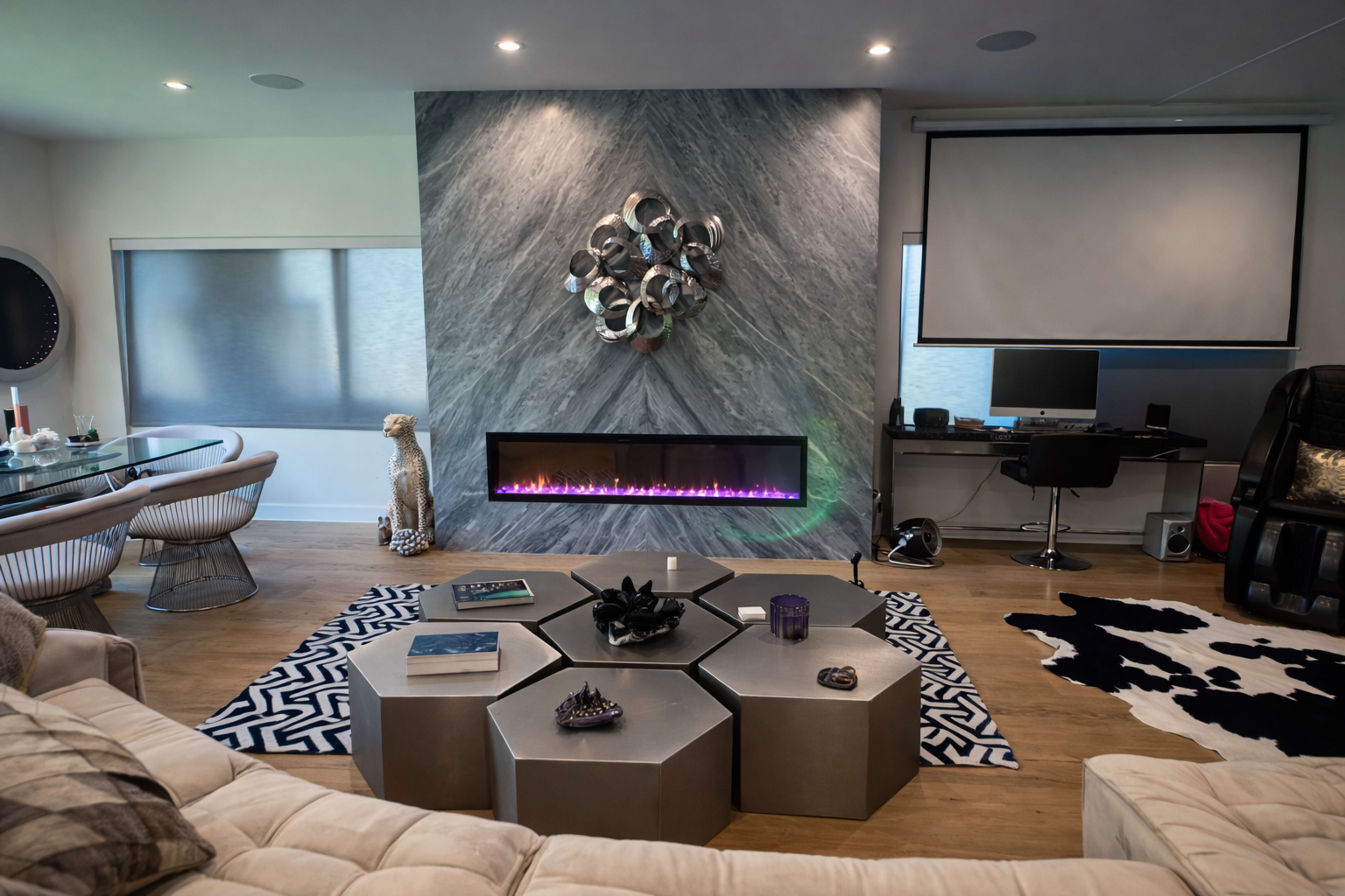 The image depicts a modern living room with a sleek fireplace, geometric coffee table, and a stylish dining area featuring a large circular table.