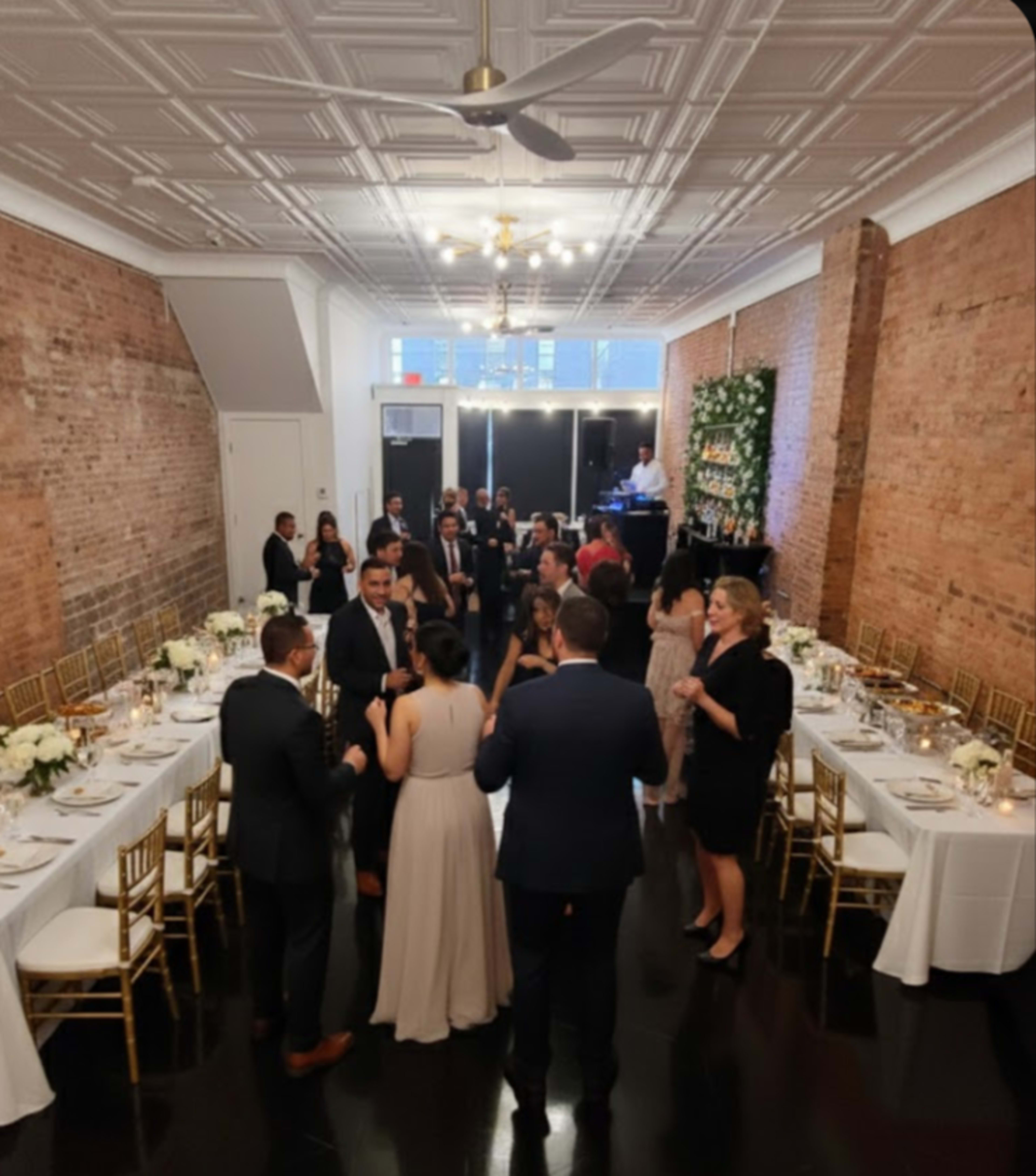 A group of guests mingles in an elegantly decorated event space featuring long dining tables set for a celebration.