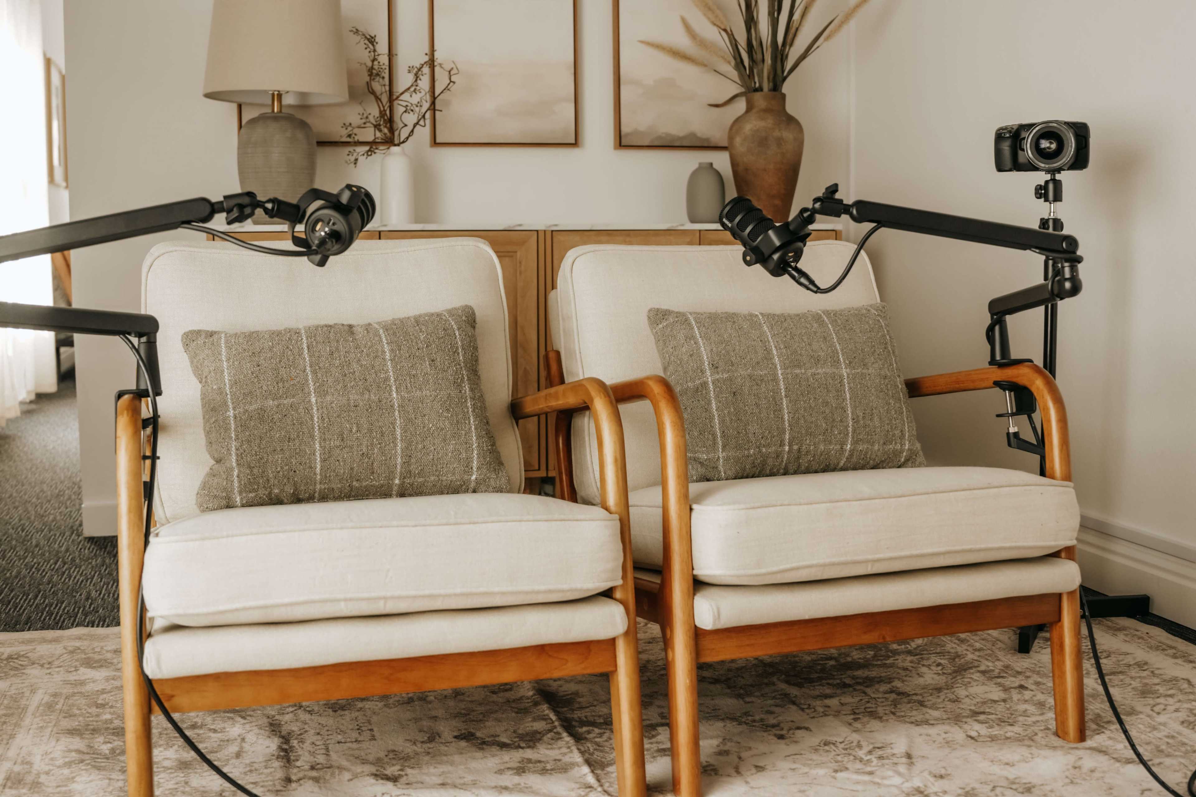 Two armchairs with beige cushions are positioned in a room with a neutral color palette, accompanied by decorative items and a camera setup on a nearby table.
