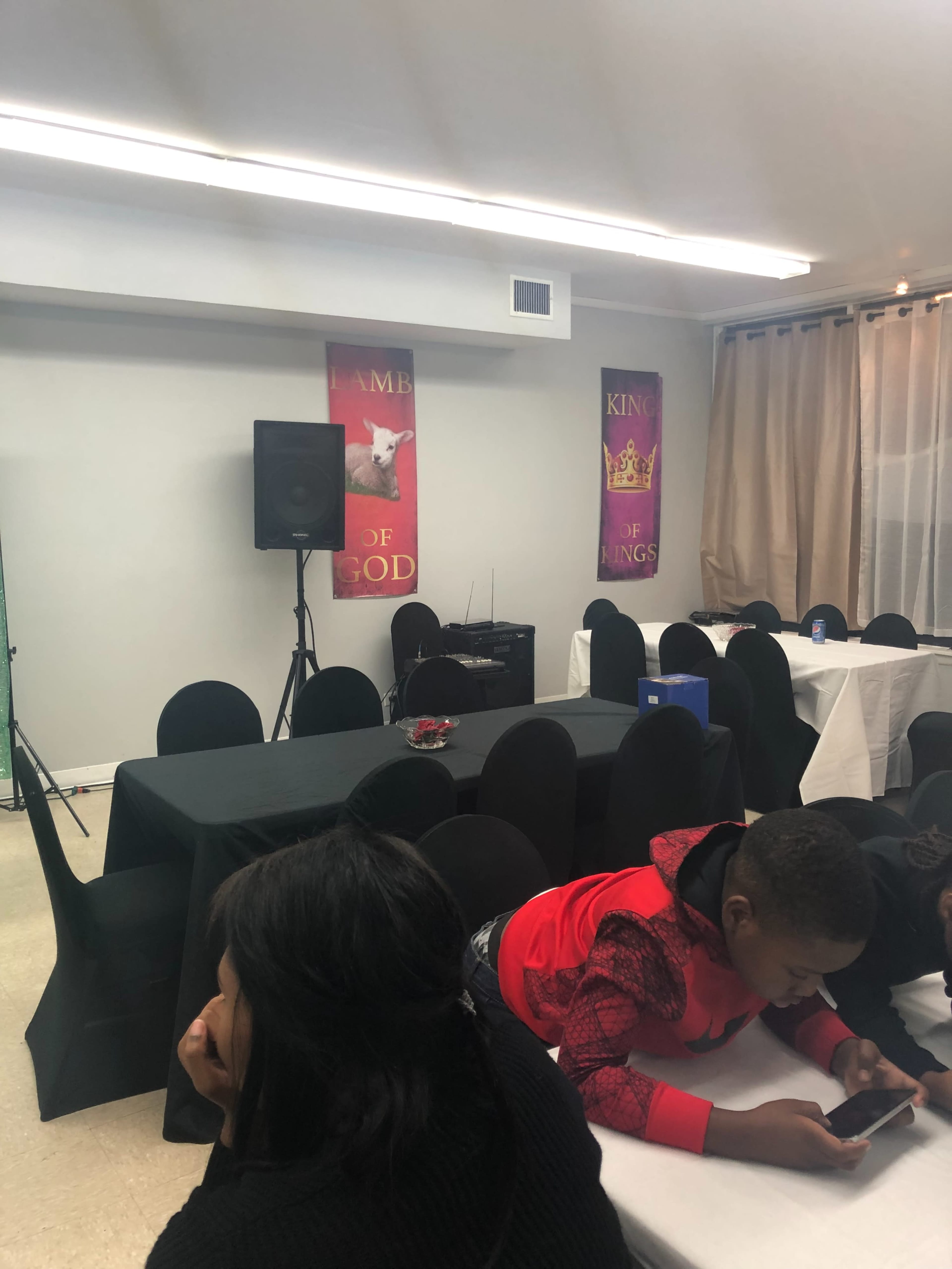 The image shows a partially set room with black and white tablecloths, a speaker, and banners depicting religious themes on the walls.