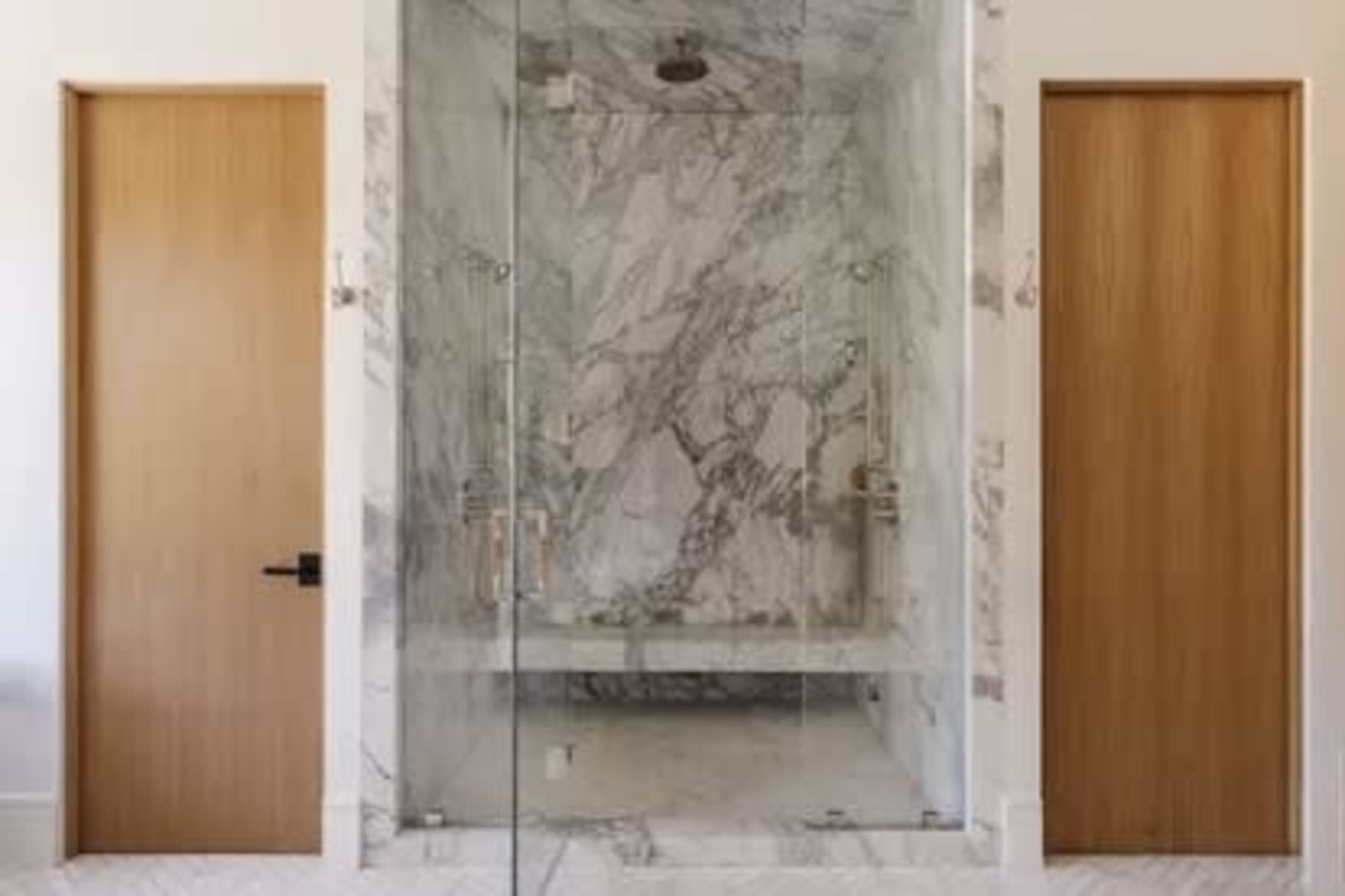 The image shows a marble shower enclosure with glass doors flanked by two wooden doors.