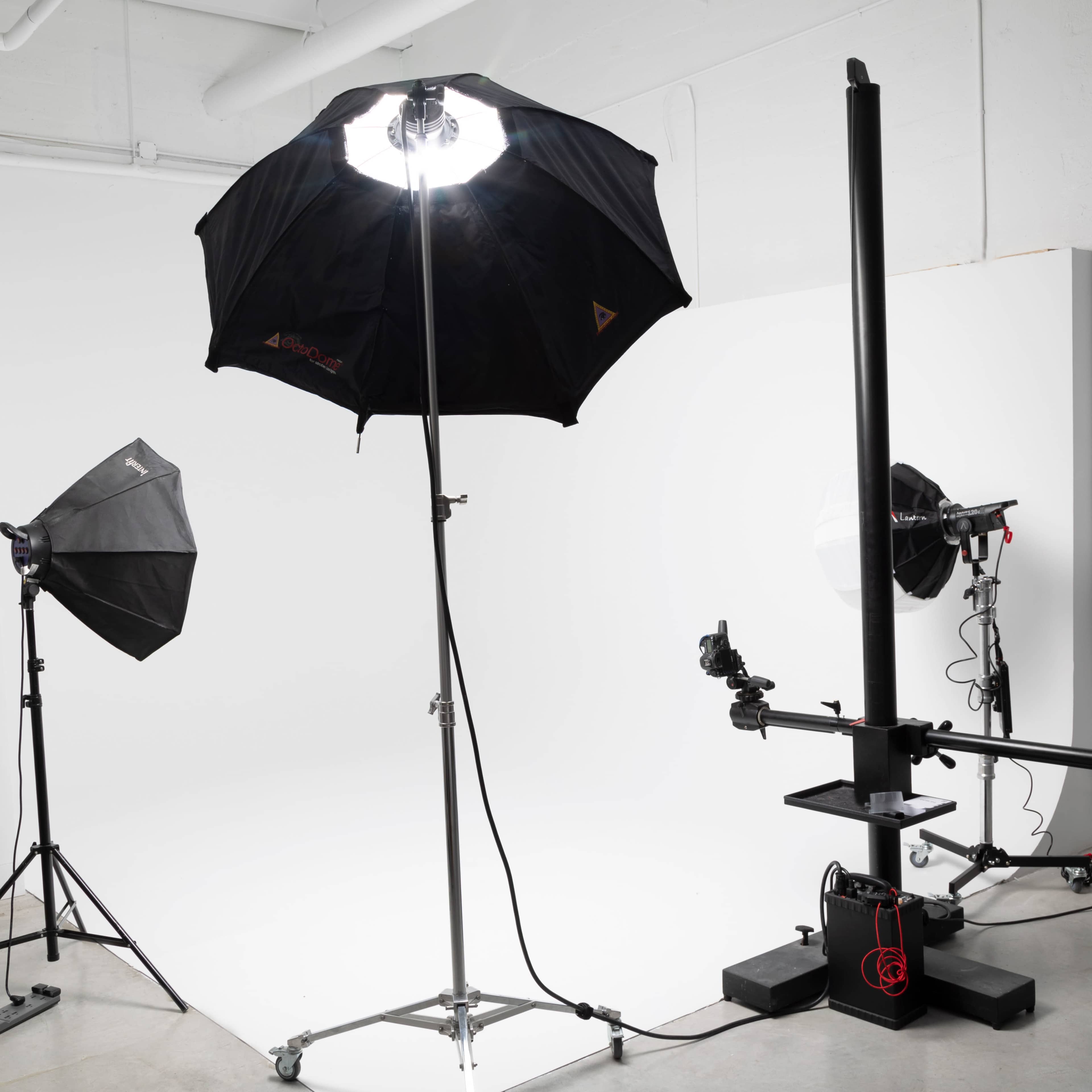 A photography studio setup with a large softbox light on a stand alongside two other light sources and a camera rig on a platform.