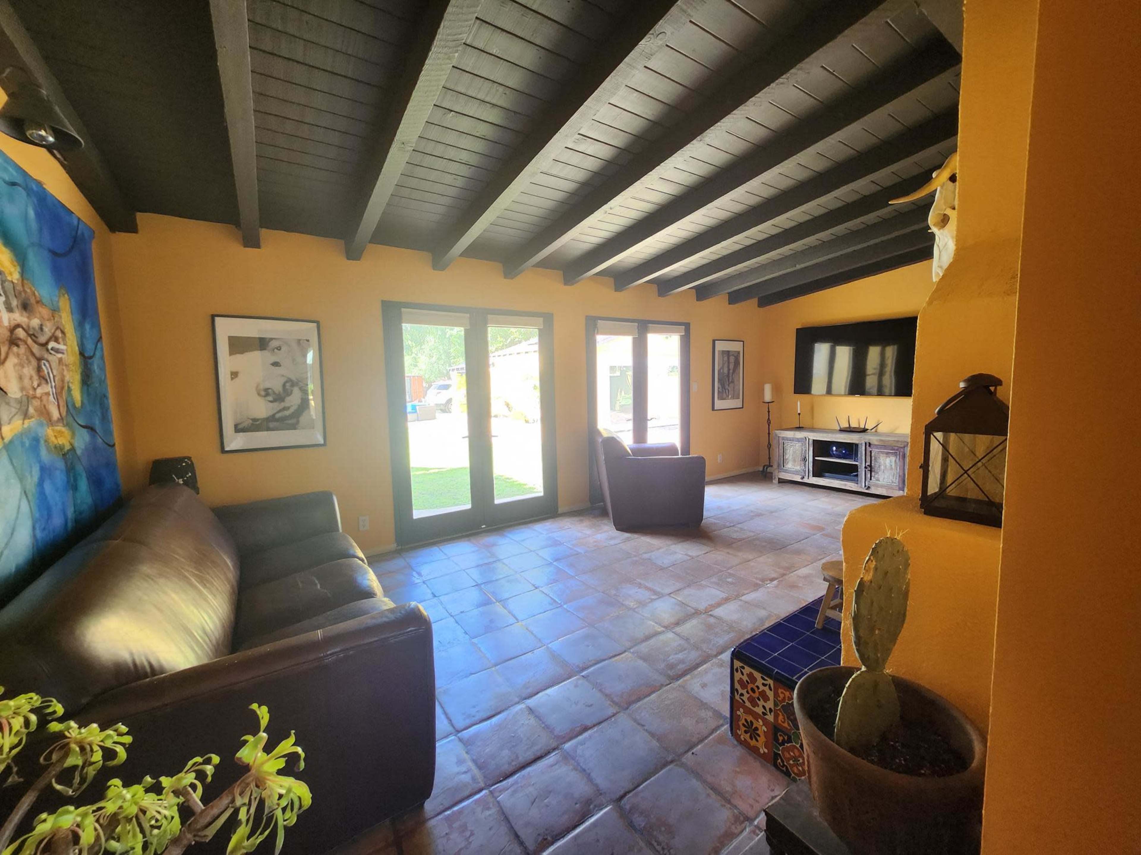 The living room features a leather sofa, two armchairs, and a television, with tiled flooring and exposed wooden beams overhead.