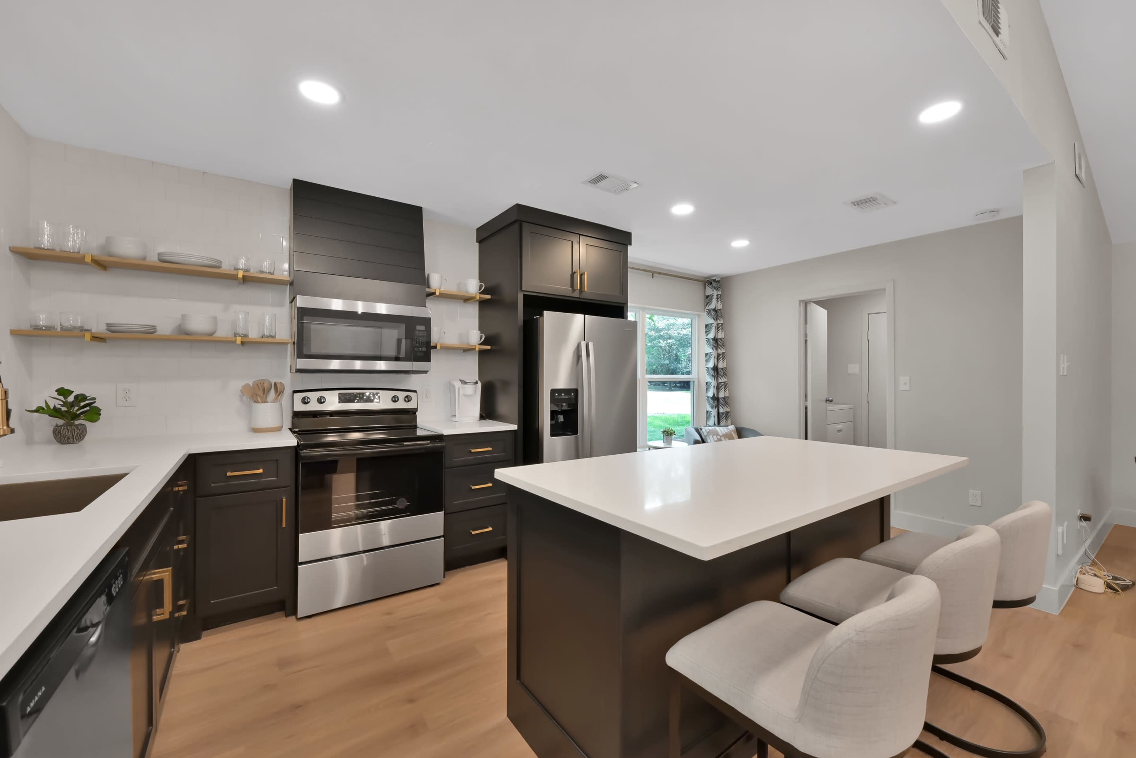 A modern kitchen with stainless steel appliances, dark cabinetry, a white countertop, and a central island with seating.