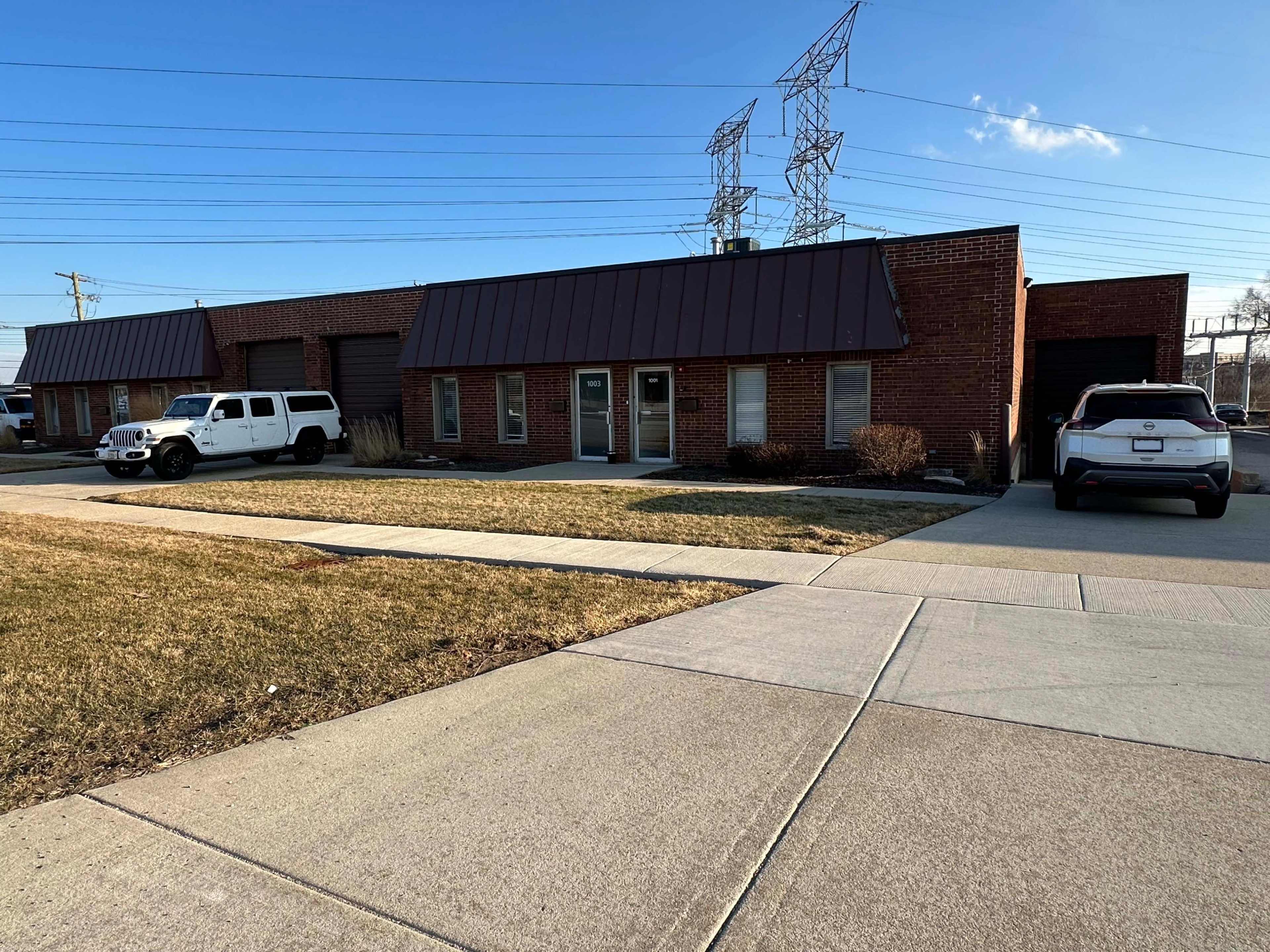 A single-story brick building with two parked vehicles in front, set against a clear blue sky and power lines.
