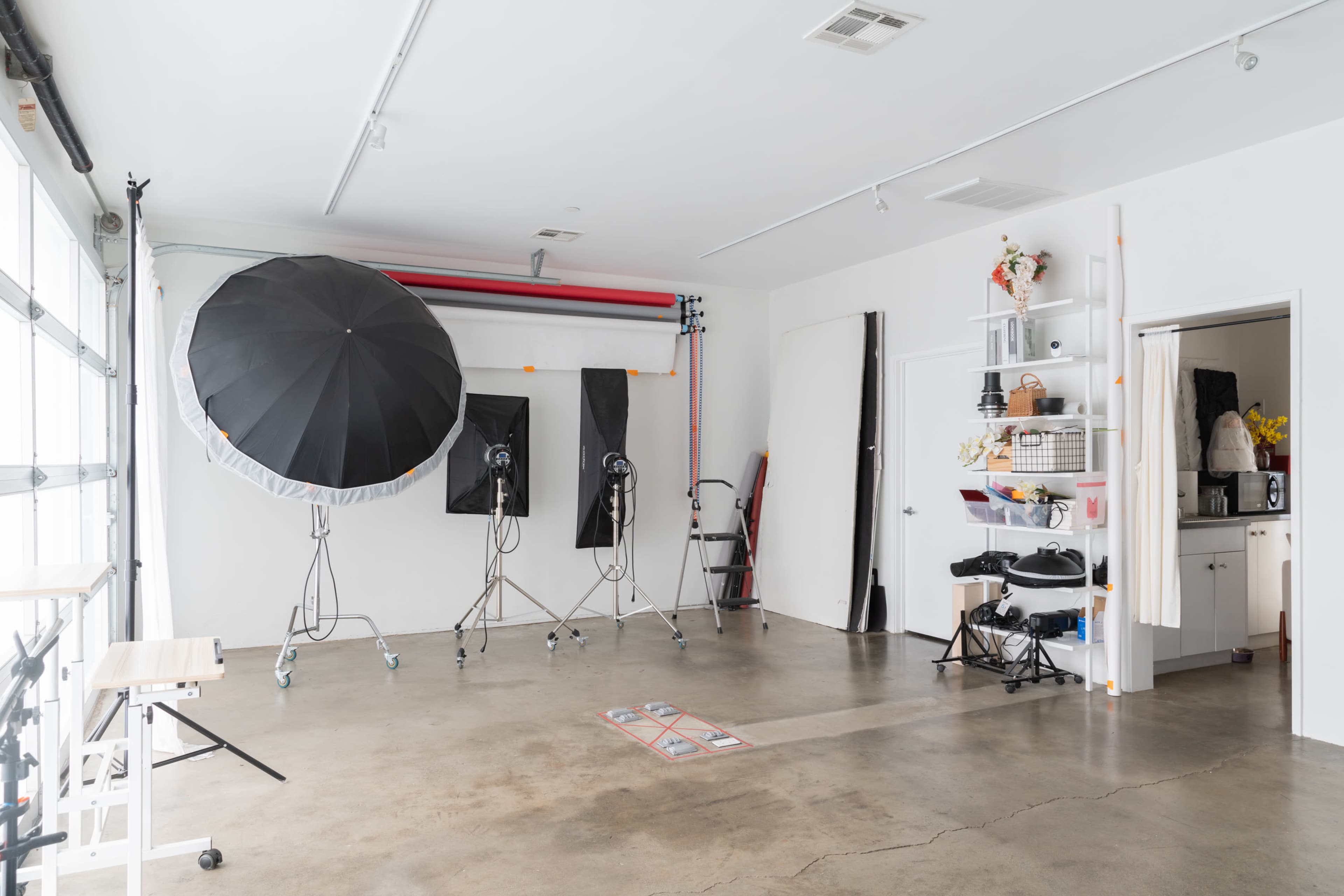 A photography studio featuring large lighting umbrellas, backdrops, and various equipment along with storage shelves.