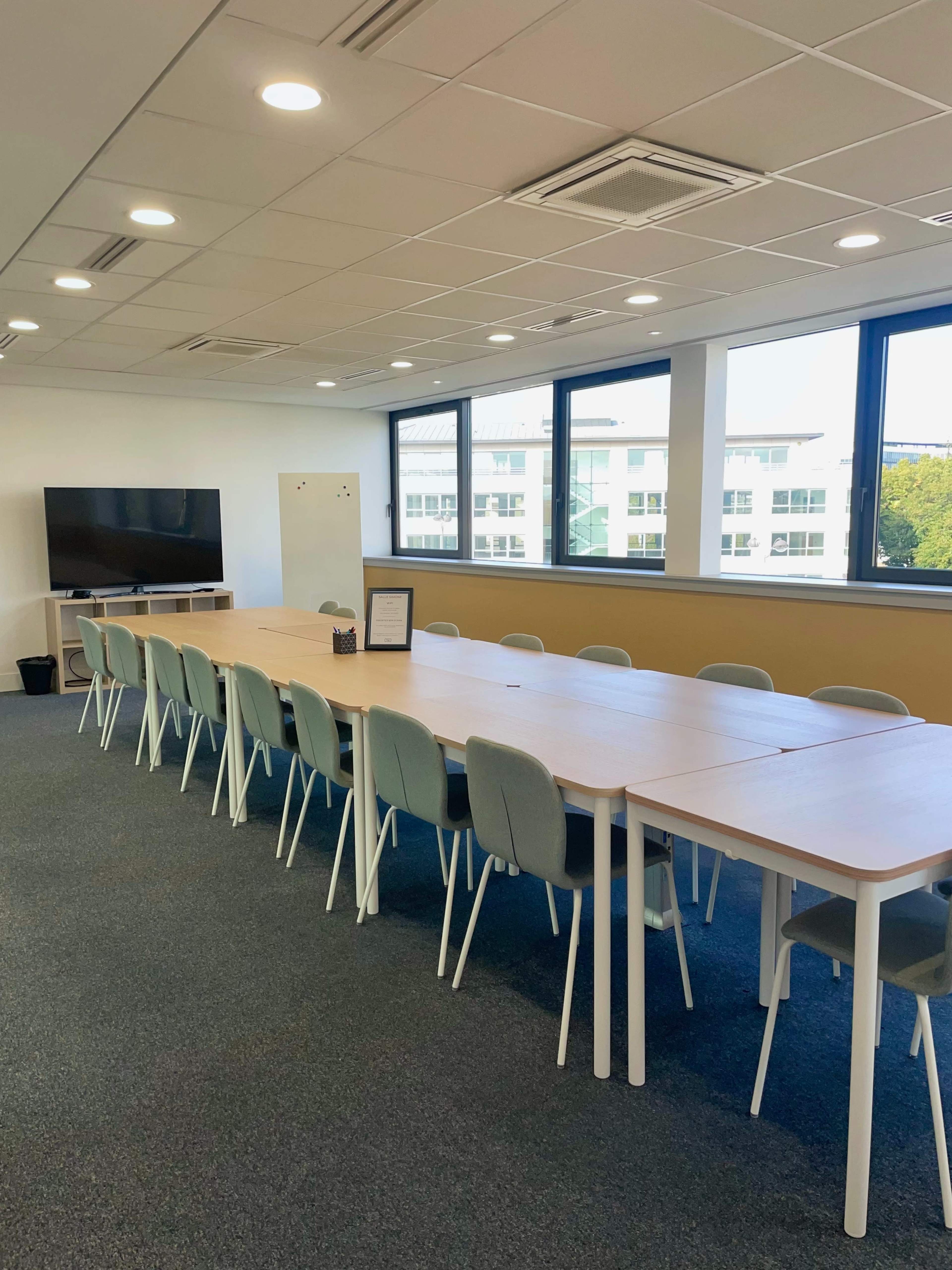 A large, modern meeting room features a long table with multiple chairs and a television mounted on the wall.