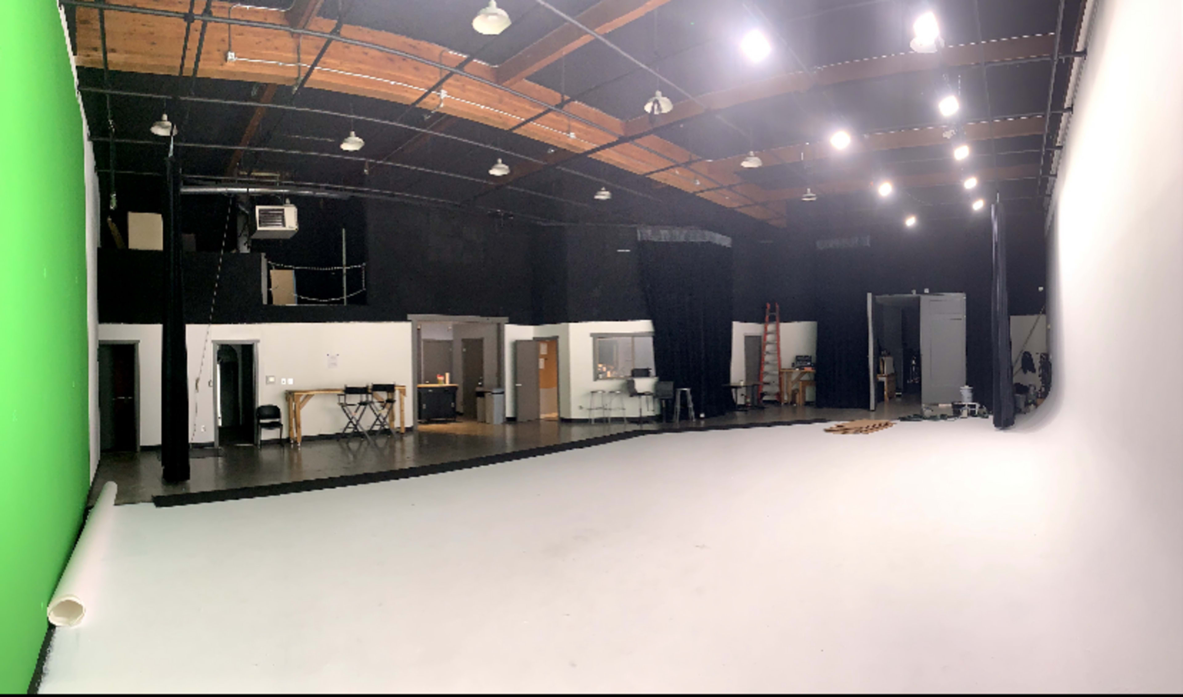 The image shows a spacious film studio with a green screen on one side and a white backdrop on the other, featuring various lighting fixtures and equipment along the walls.