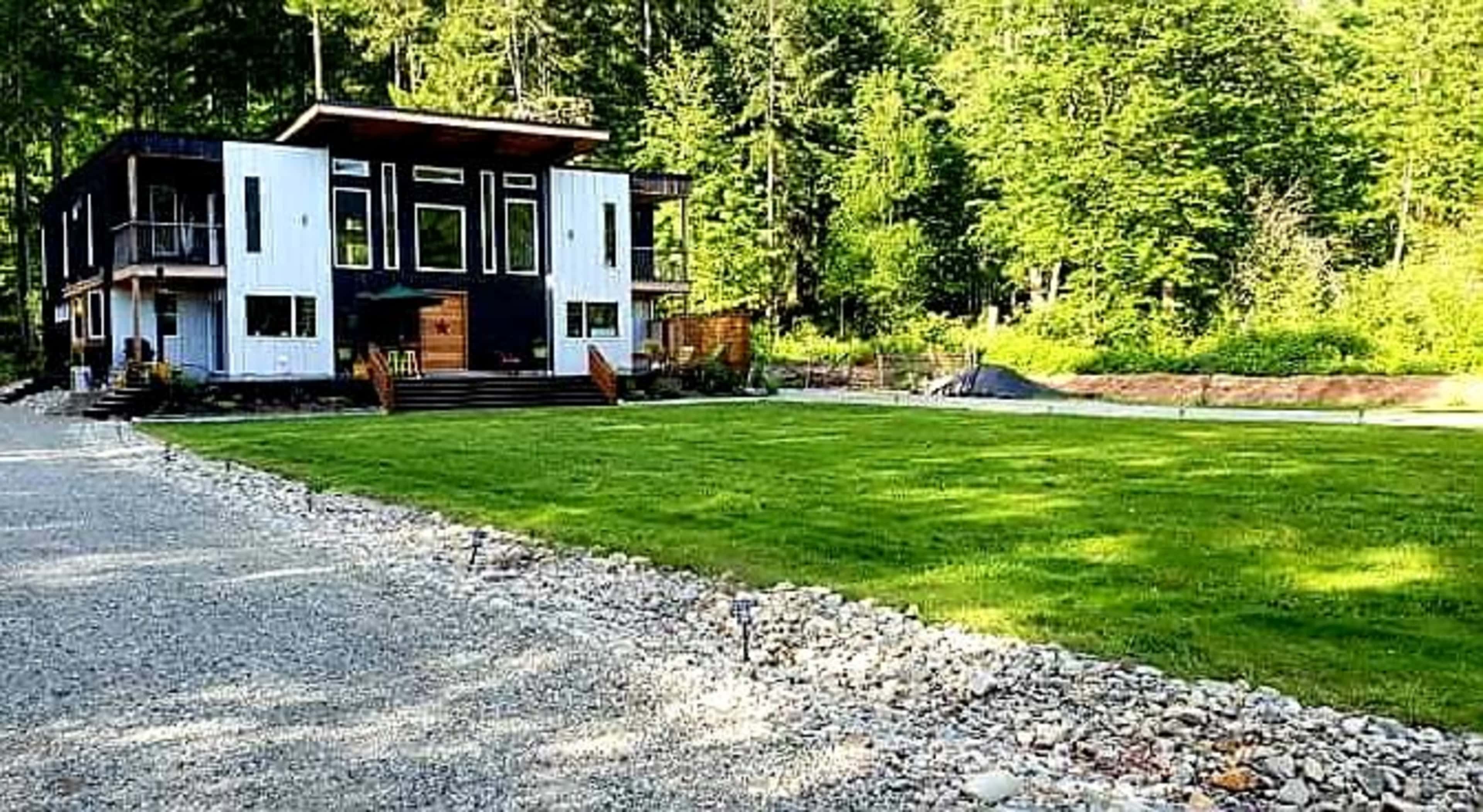 A modern two-story house with a black and white exterior is situated on a grassy lawn surrounded by trees.