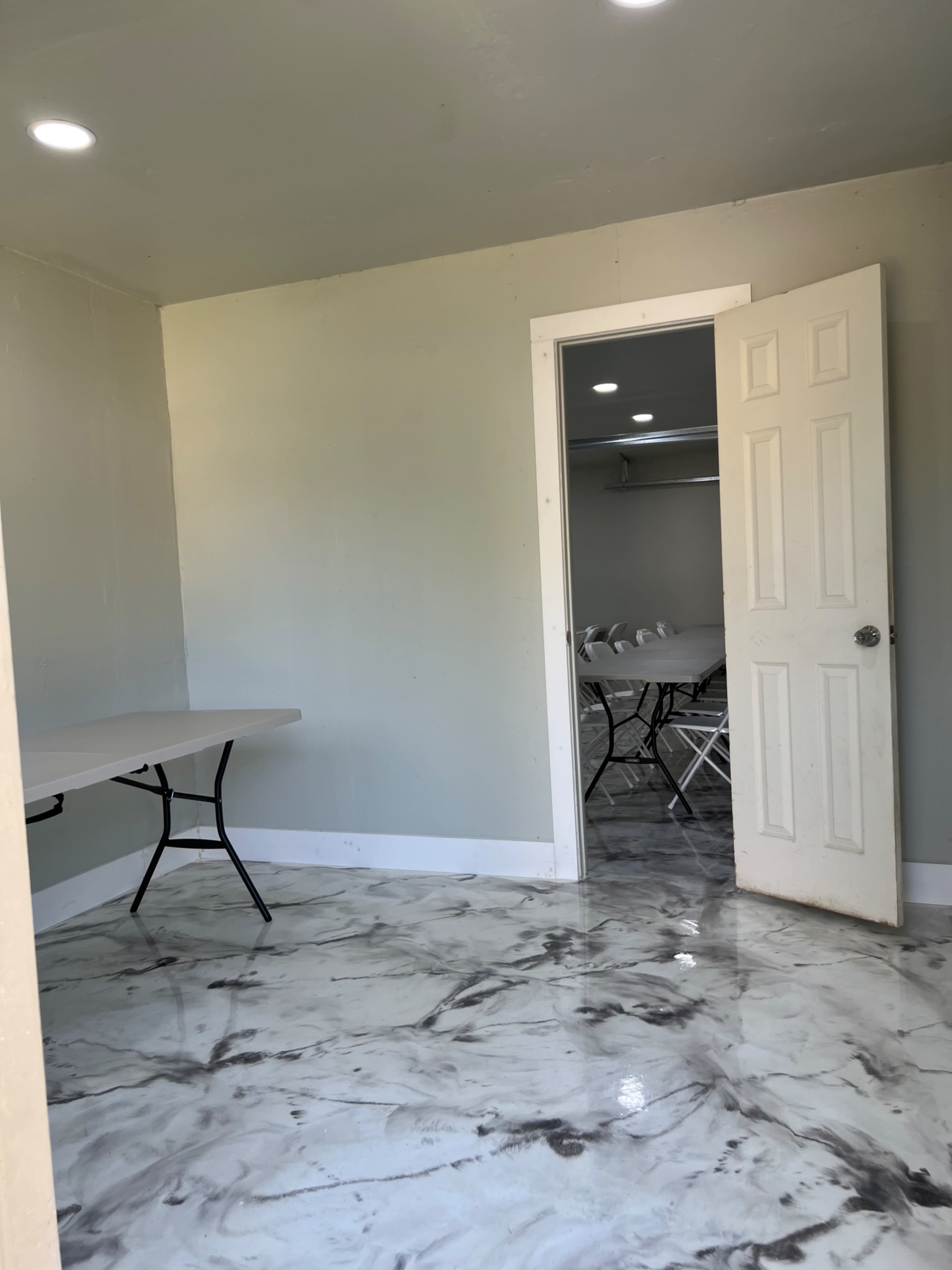 An empty room with a light-colored wall, a table on the left, and an open door leading to another room in the background.
