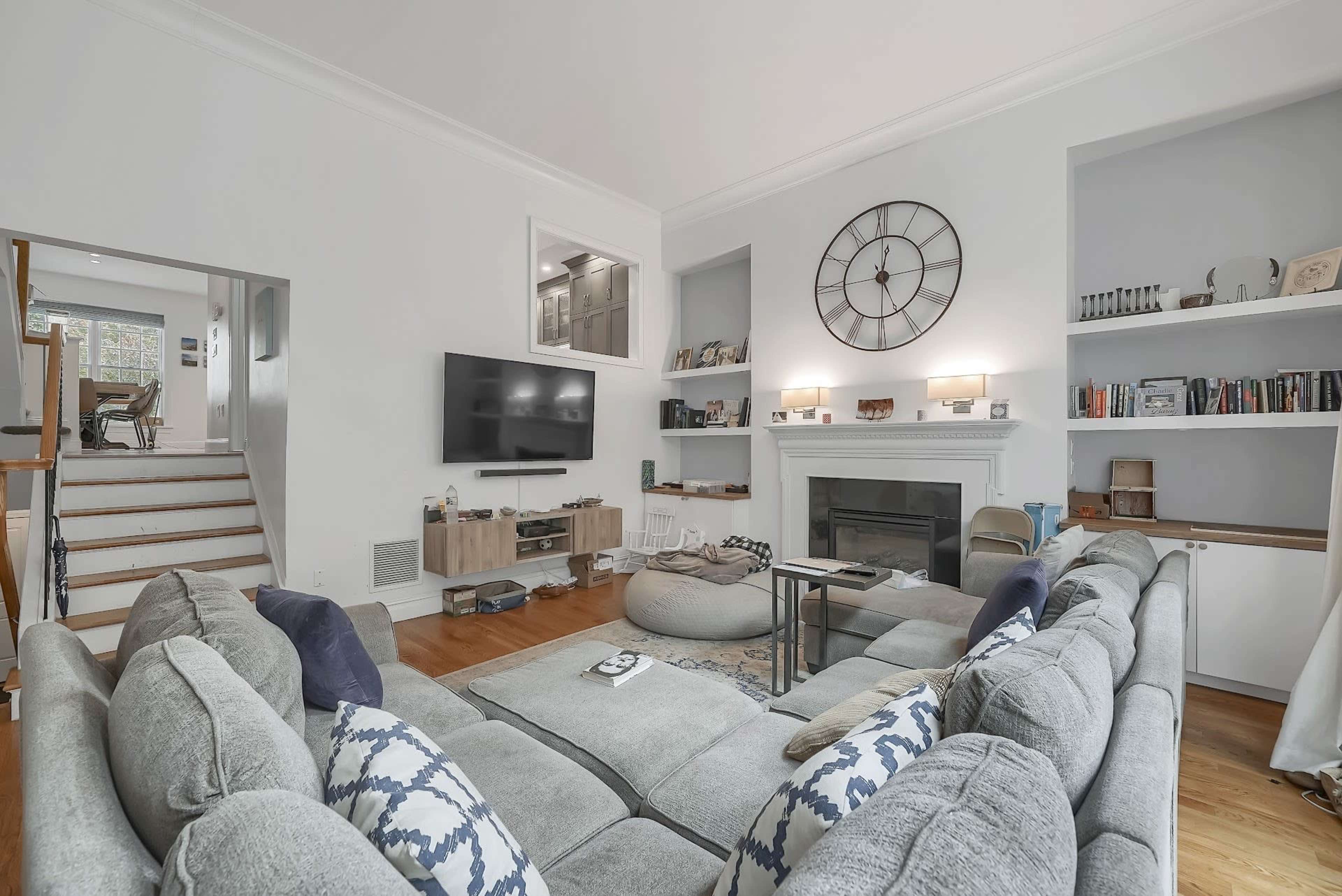 A spacious living room with a large sectional sofa, a wall-mounted television, a fireplace, and shelves filled with books and decorative items.