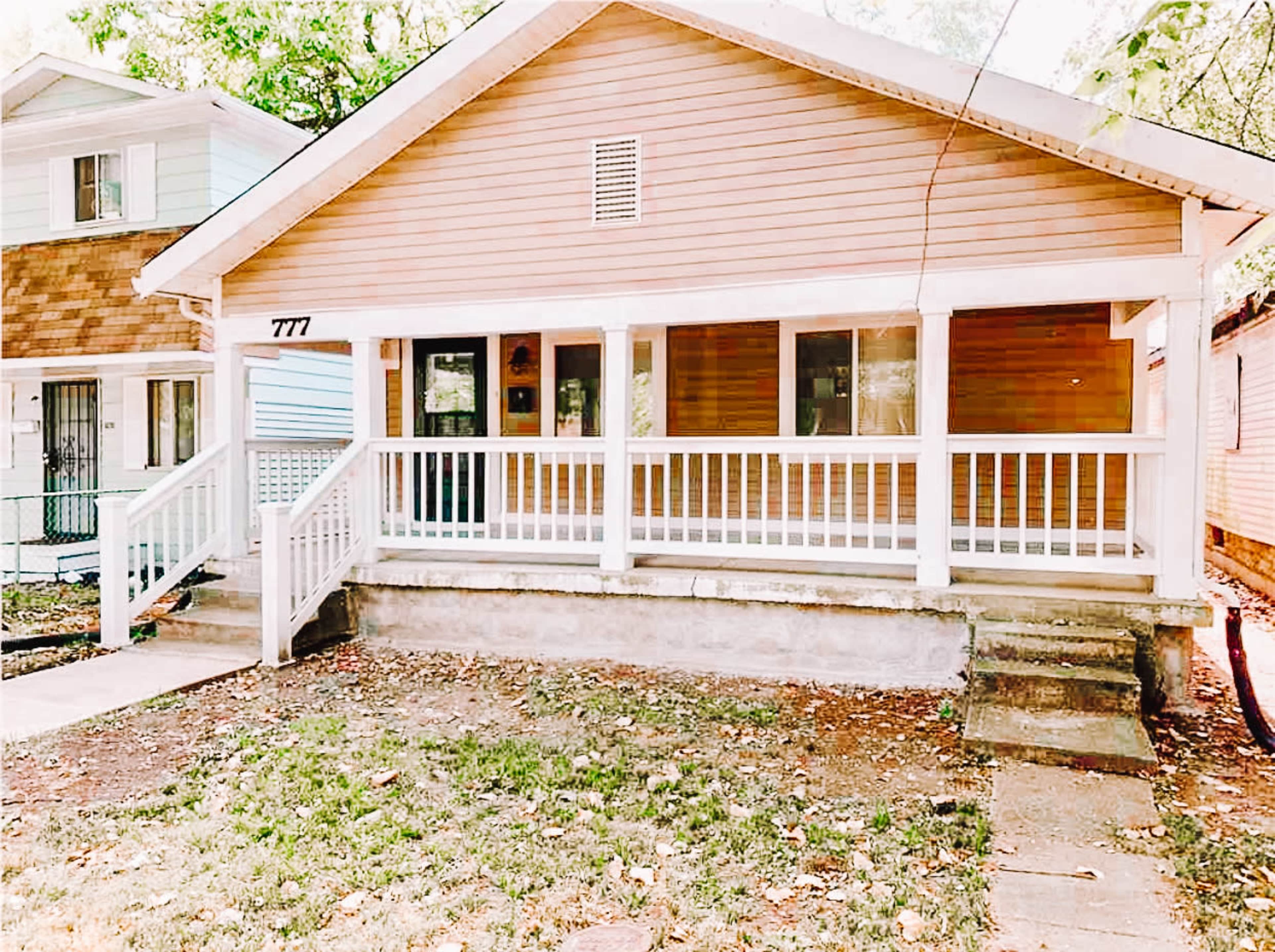 A single-story house with a wooden exterior and a front porch surrounded by a grassy area and a few trees.