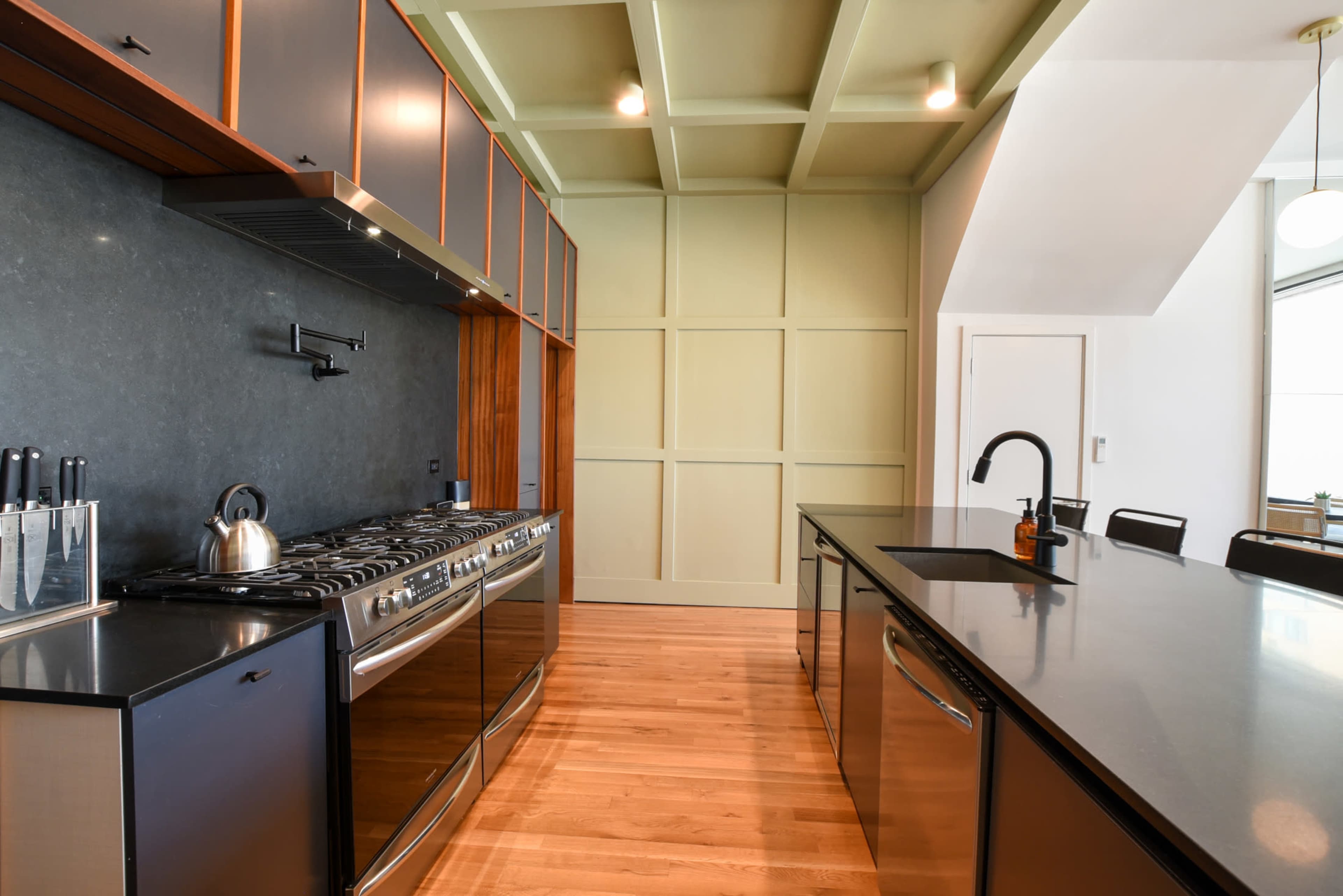 A modern kitchen features a stainless steel range, dark cabinetry, and a spacious island with a black countertop.