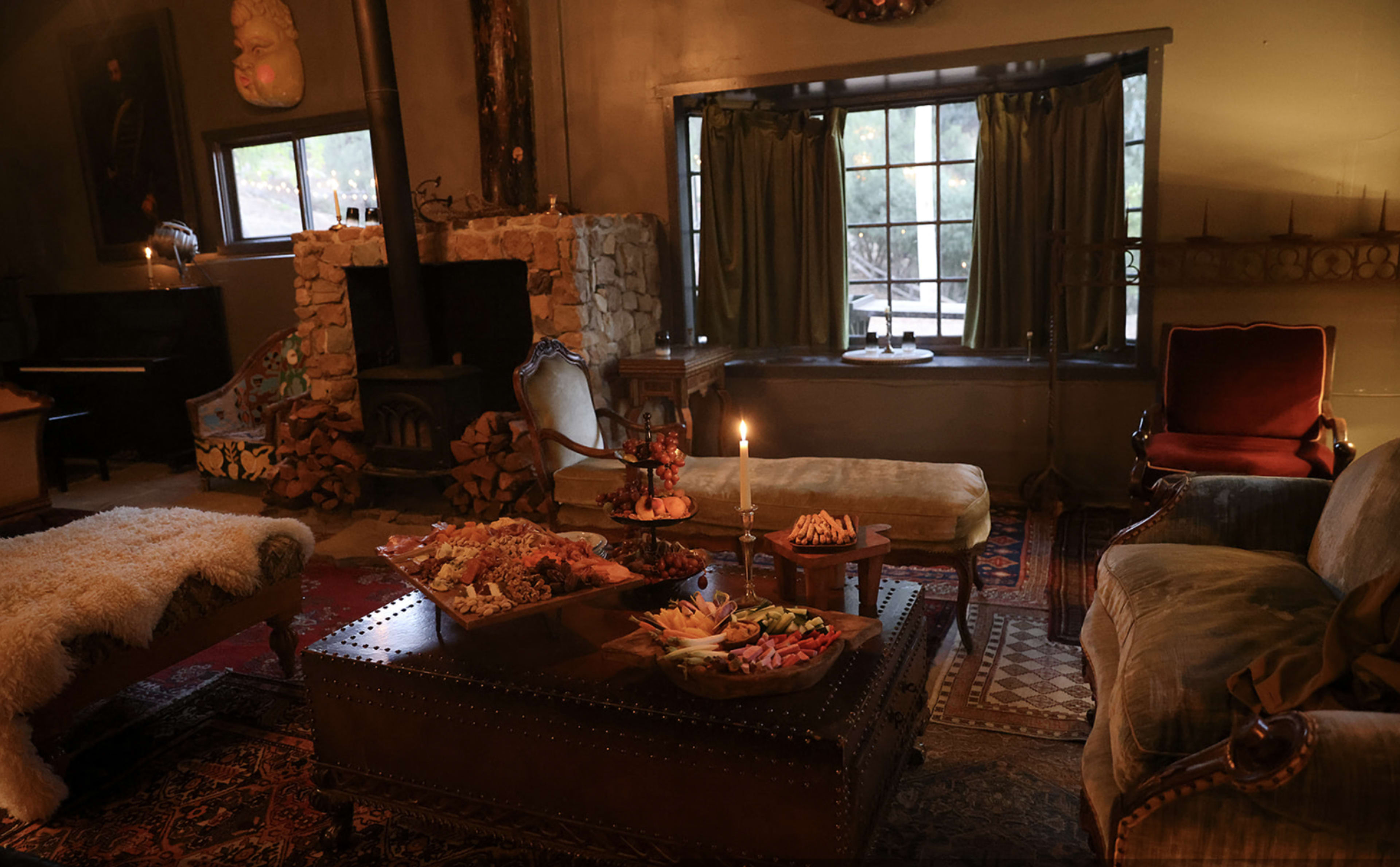 A cozy living room with a stone fireplace, decorative seating, and a table filled with an assortment of snacks.