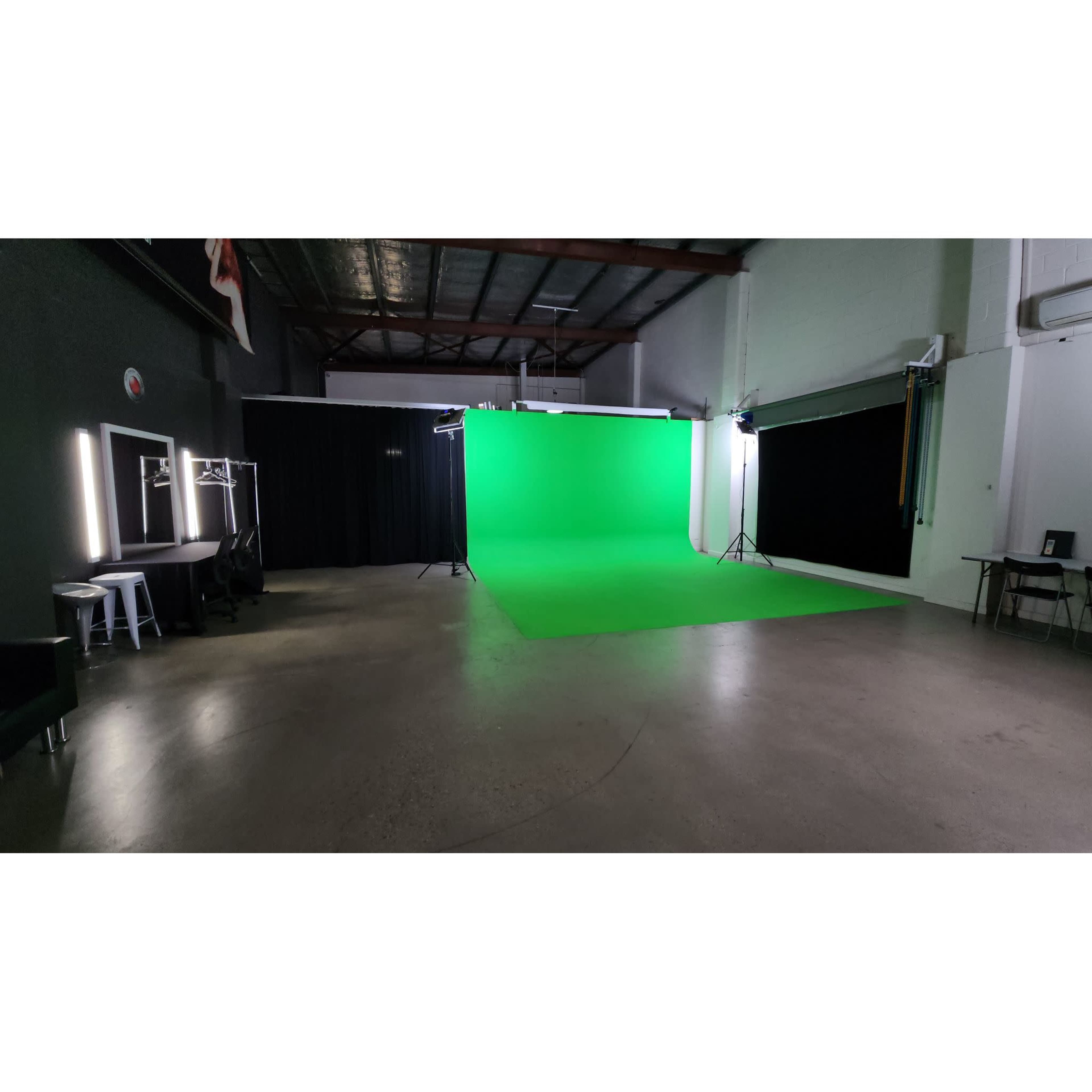 The image shows an empty studio space featuring a green backdrop and various lighting equipment set up for video production.