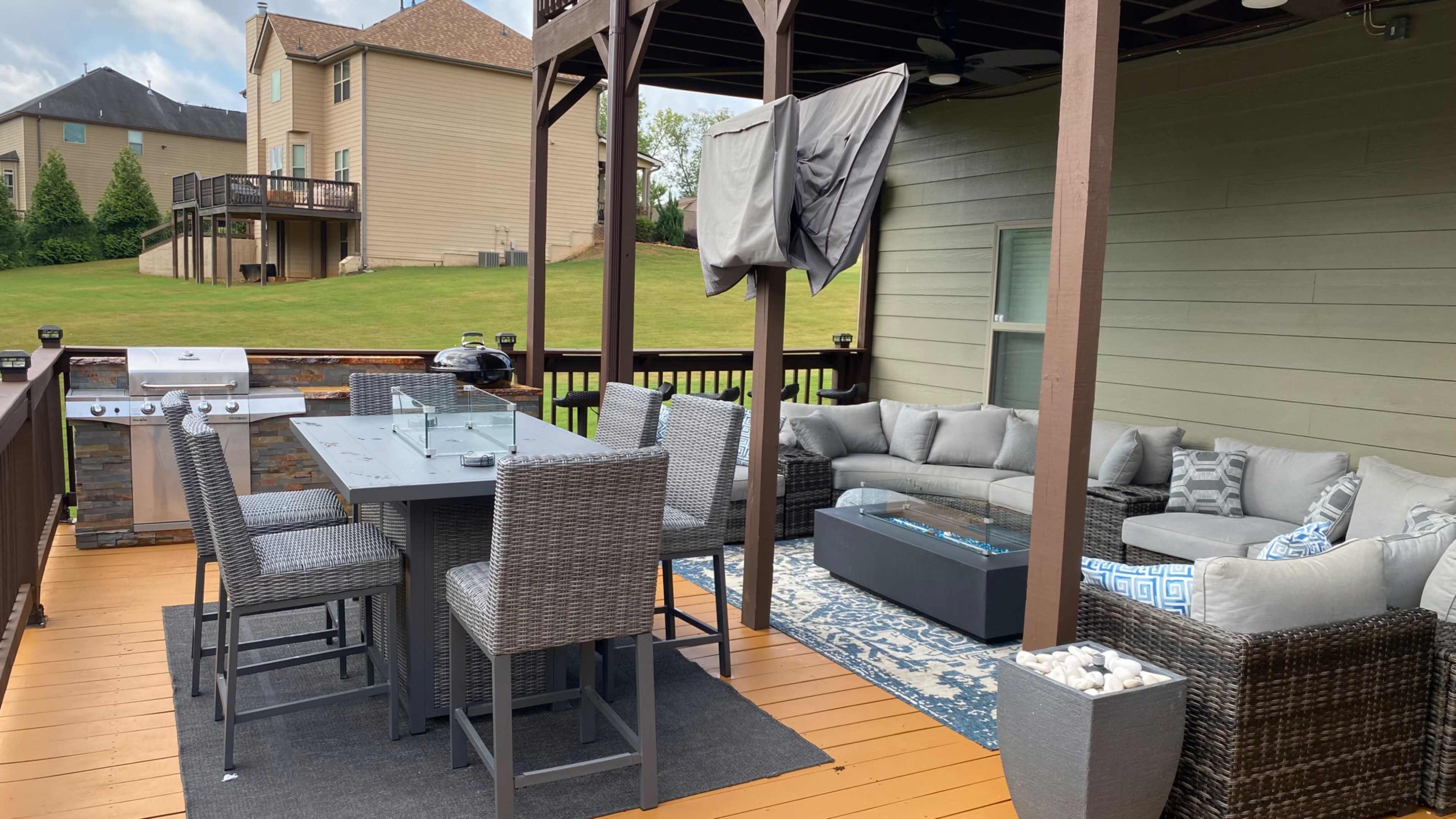 A patio area with a dining table, chairs, and a seating arrangement under a pergola, along with a grill and decorative elements.