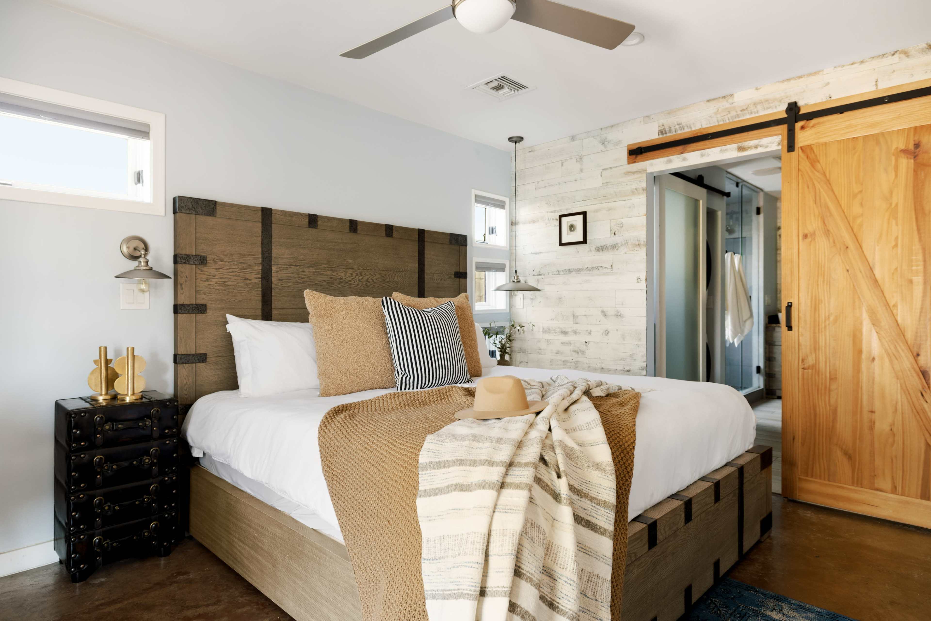 The bedroom features a large bed with a wooden headboard, a cozy throw on the bed, and a sliding barn door leading to an adjoining room.